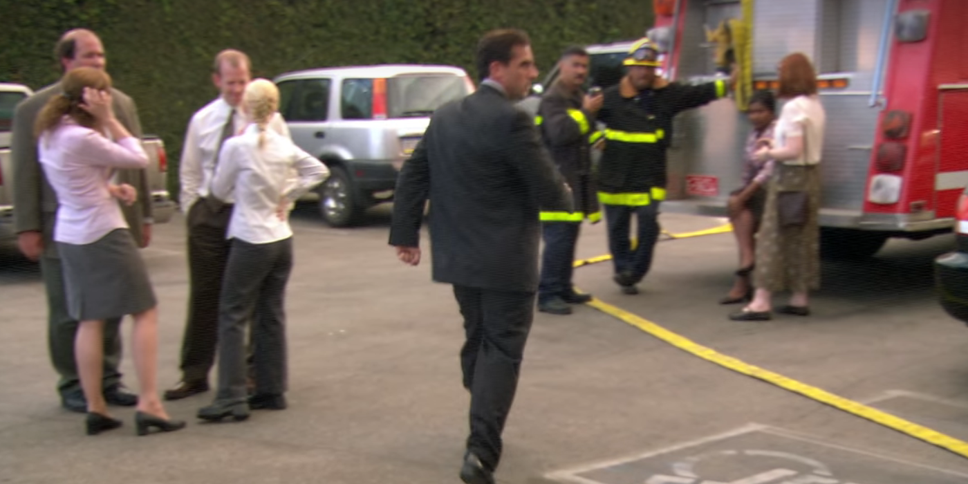 Meredith e Kelly flertando com os bombeiros ao fundo enquanto Michael corre em direção a eles em The Office The Fire Episode