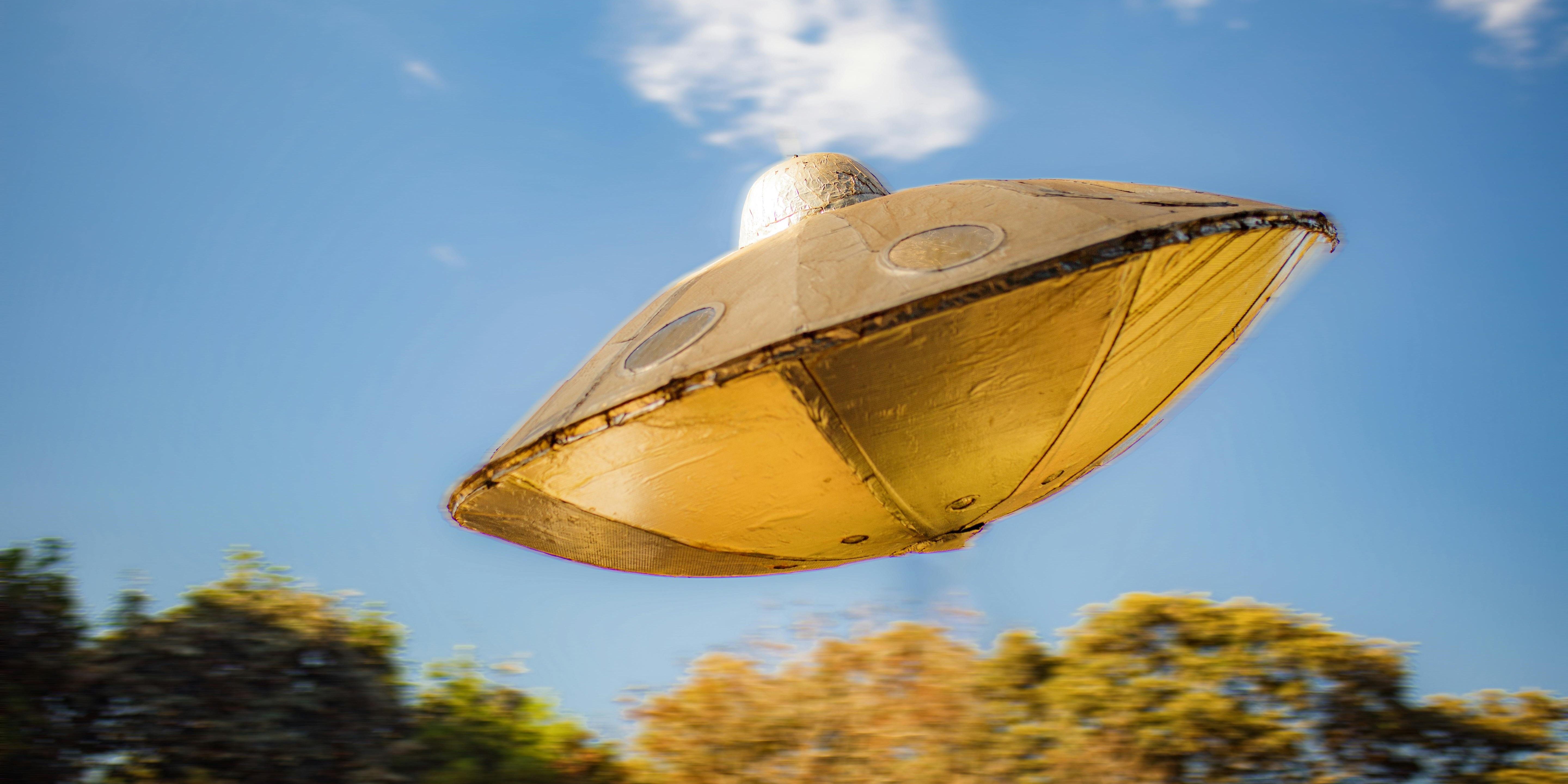 An image of a UFO flying above trees in a daytime sky
