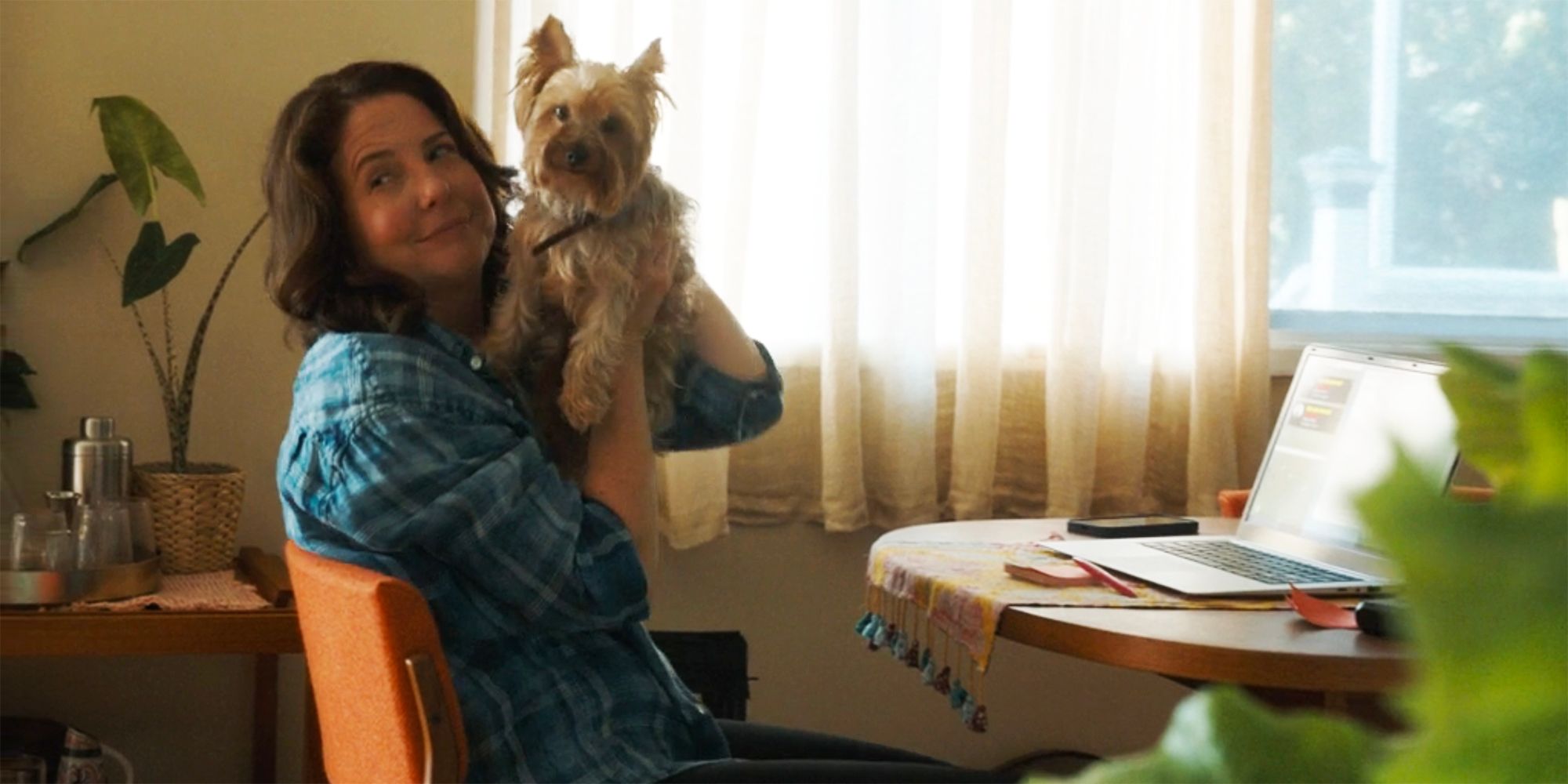 Teddi is holding up a small dog while sitting at the computer in Tracker.