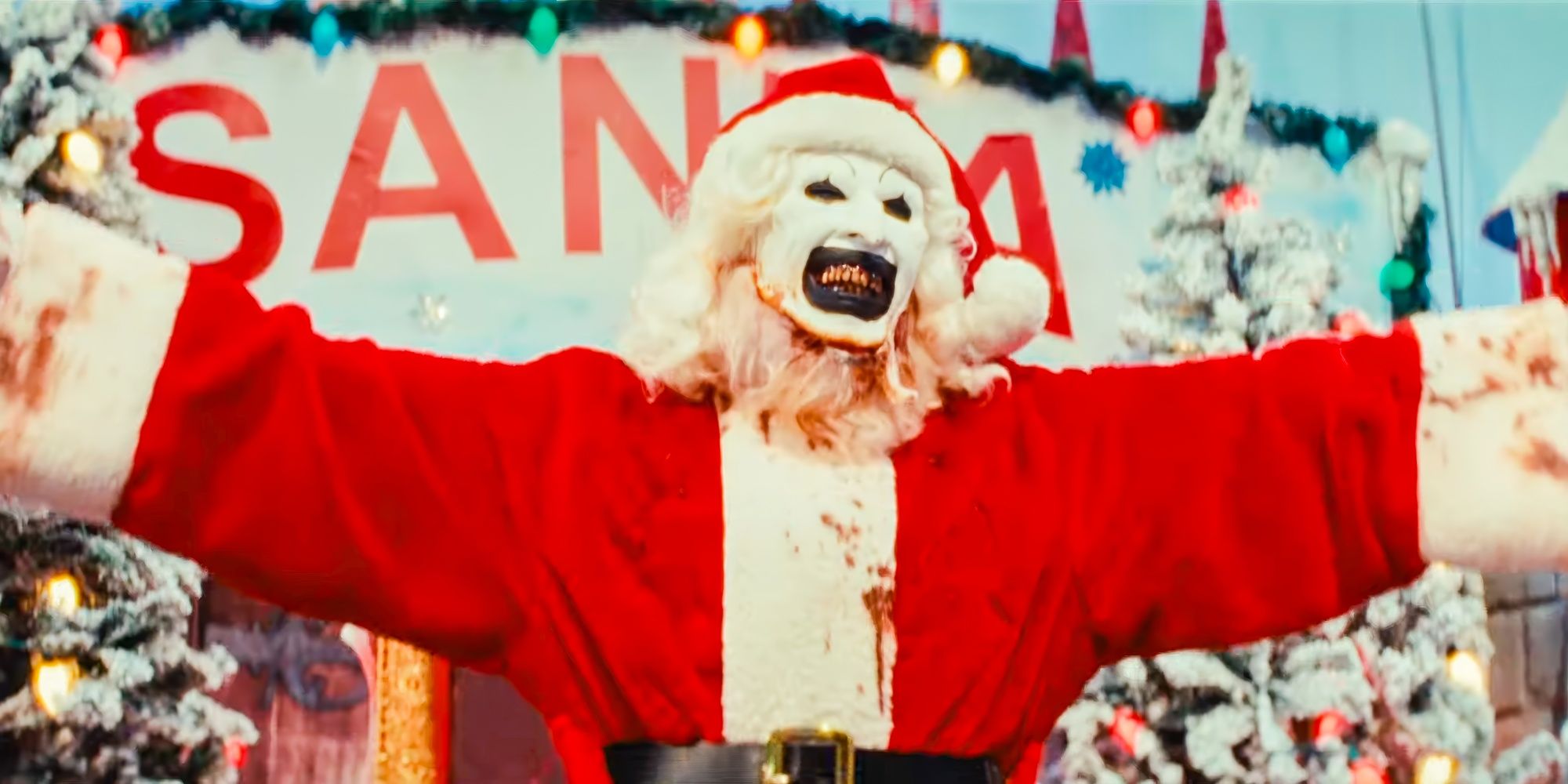 David Howard Thornton as Art The Clown dressed as santa lifting up his arms and smiling in Terrifier 3