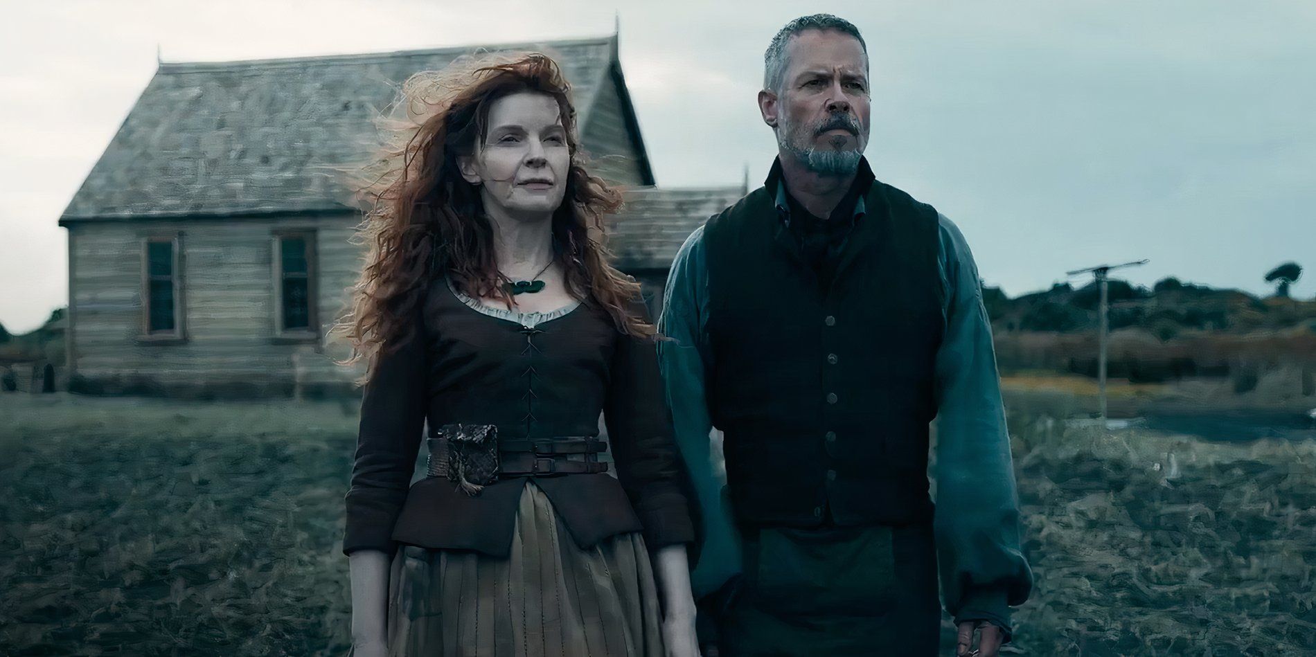Jacqueline McKenzie as Charlotte and Guy Pearce as Father Munro look into the distance in front of a rural house in The Convert