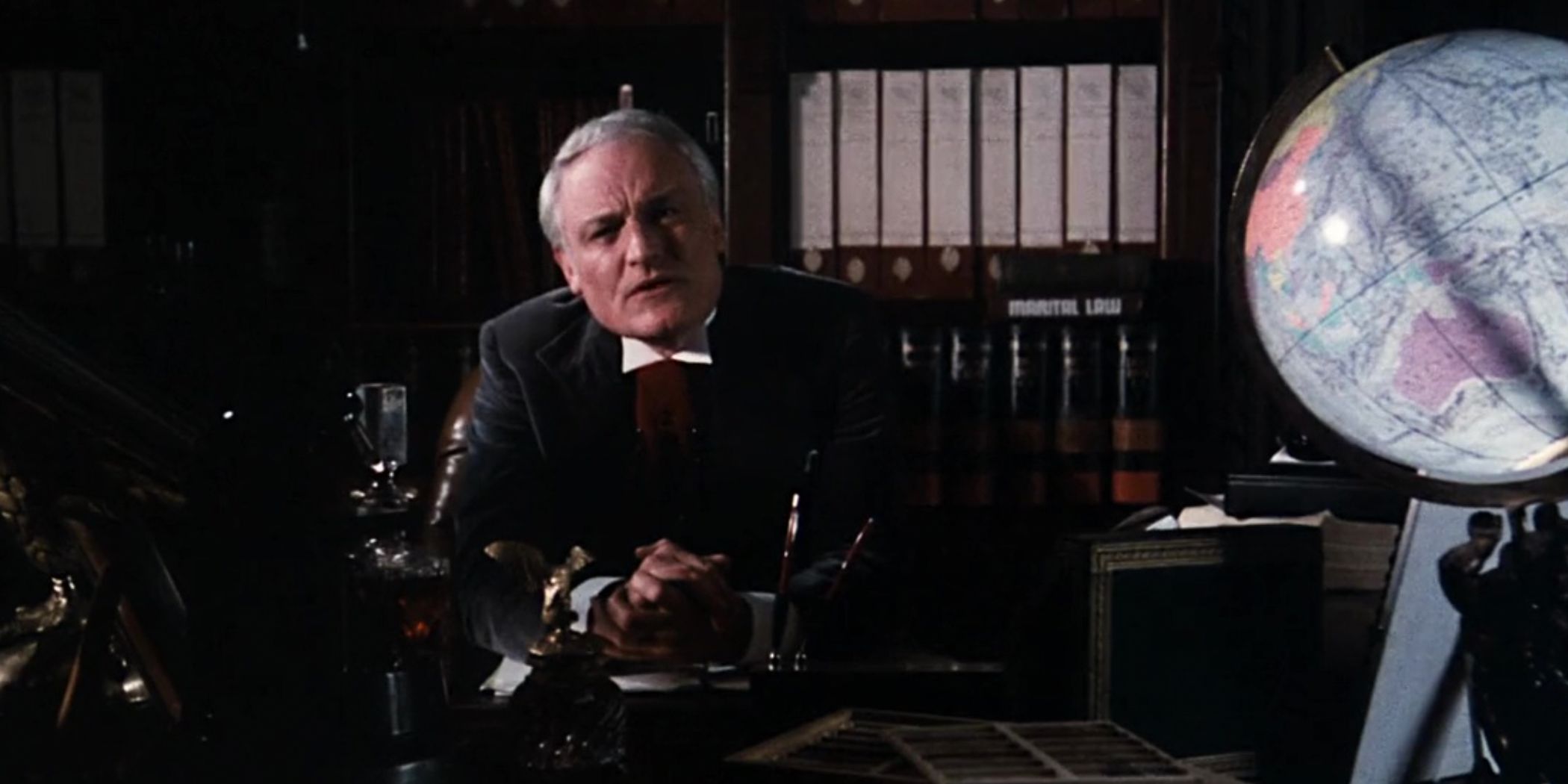 The Criminologist sitting at his desk and talking to the audience in Rocky Horror Picture Show