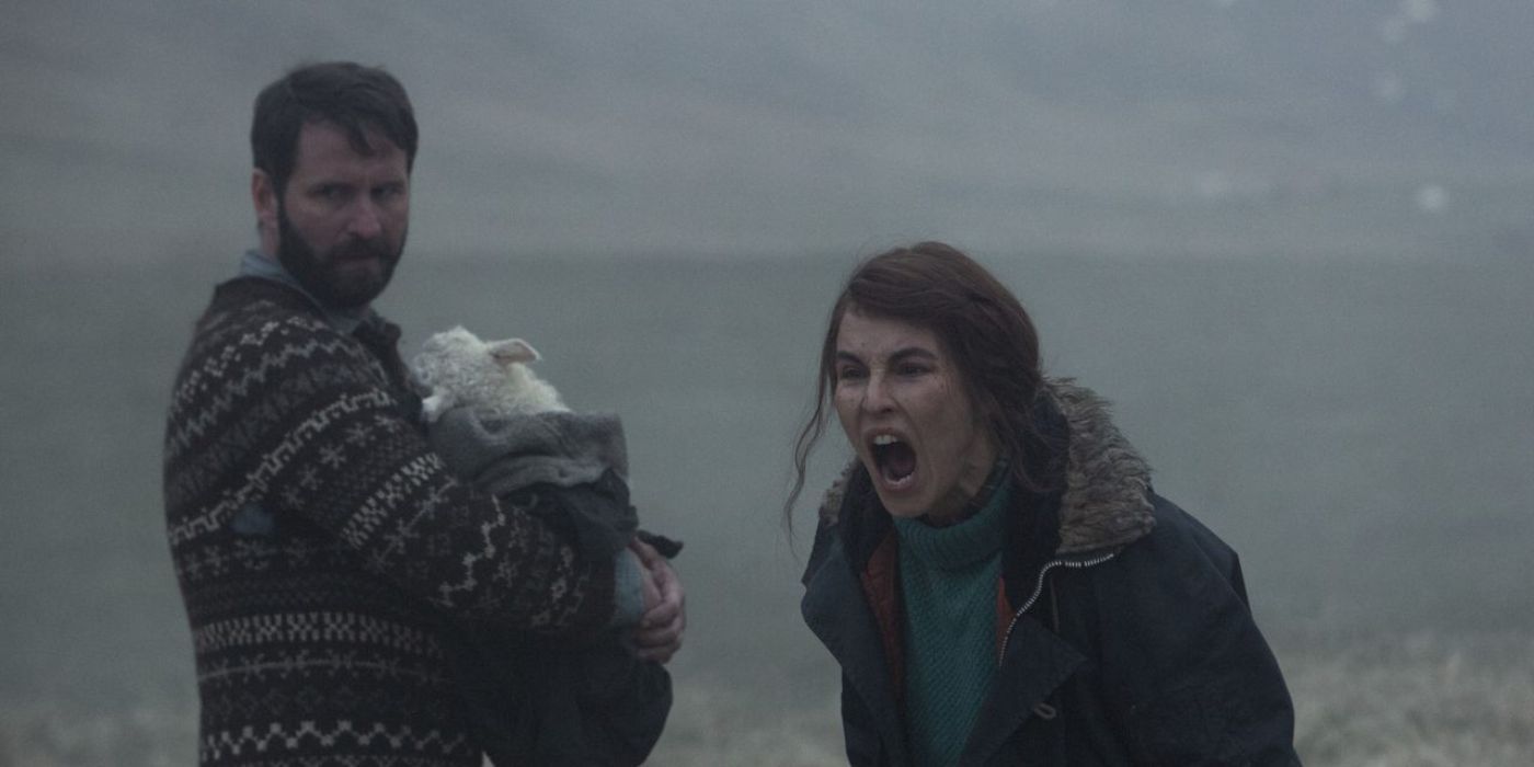 parental protectiveness in Lamb, a man holds a lamb in a blanket while a woman screams at something off screen in the icelandic landscape 