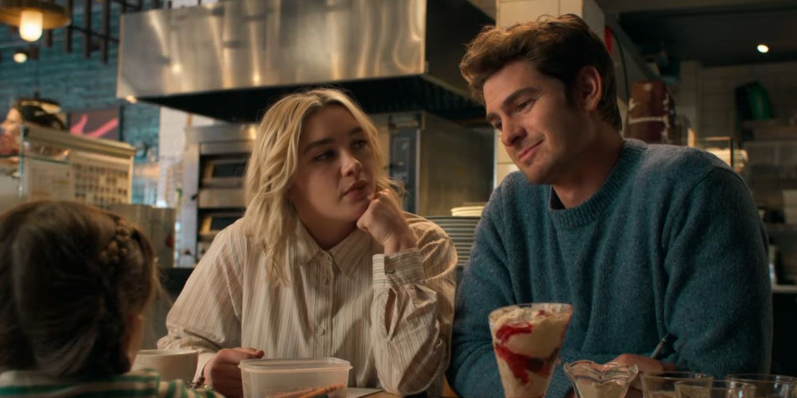 Florence Pugh and Andrew Garfield sitting at a diner eating ice cream with their on-screen daughter in We Live in Time