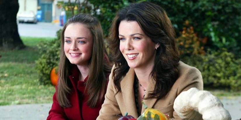 Rory (Alexis Bledel)and Lorelai Gilmore (Lauren Graham) sitting next to each other smiling on Thanksgiving in Gilmore Girls