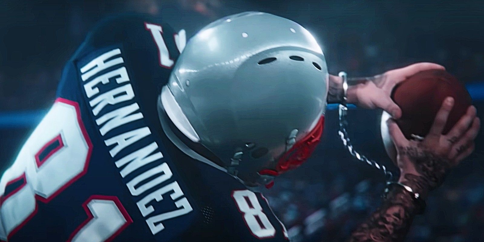a fictionalized version of Aaron Hernandez catches a football while facing away from the camera, though his wrists are handcuffed
