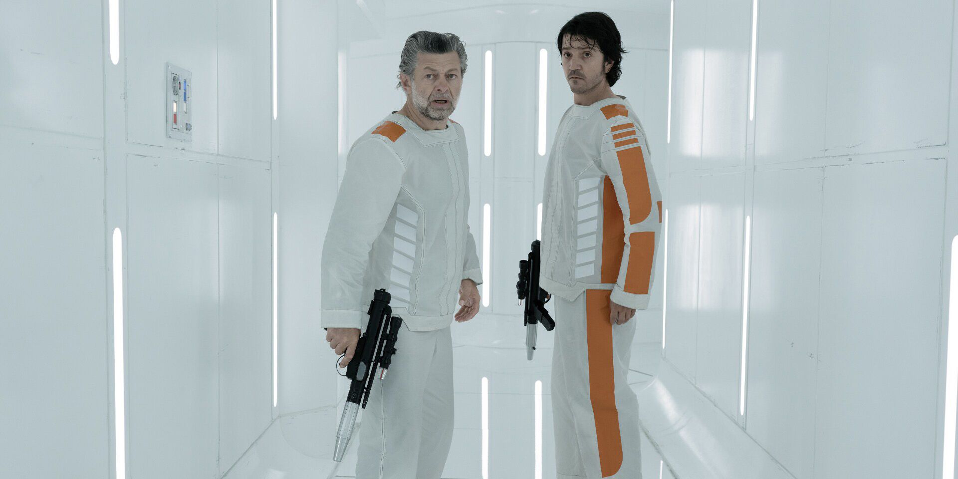 Andy Serkis and Diego Luna holding guns in front of a white wall in Andor