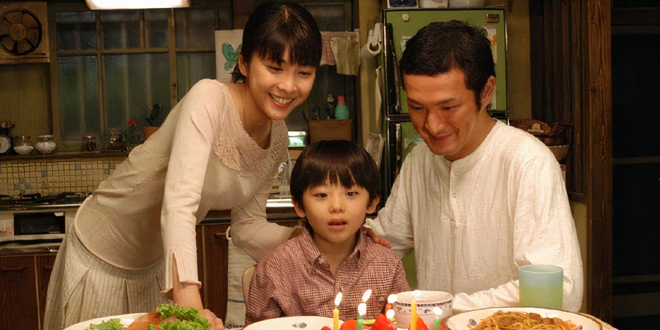 Mio and Takumi stand next to Yuji as he blows candles out on his cake. 