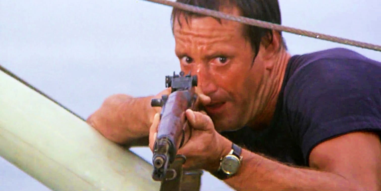 Brody aiming a gun at the shark while laying on the mast in Jaws