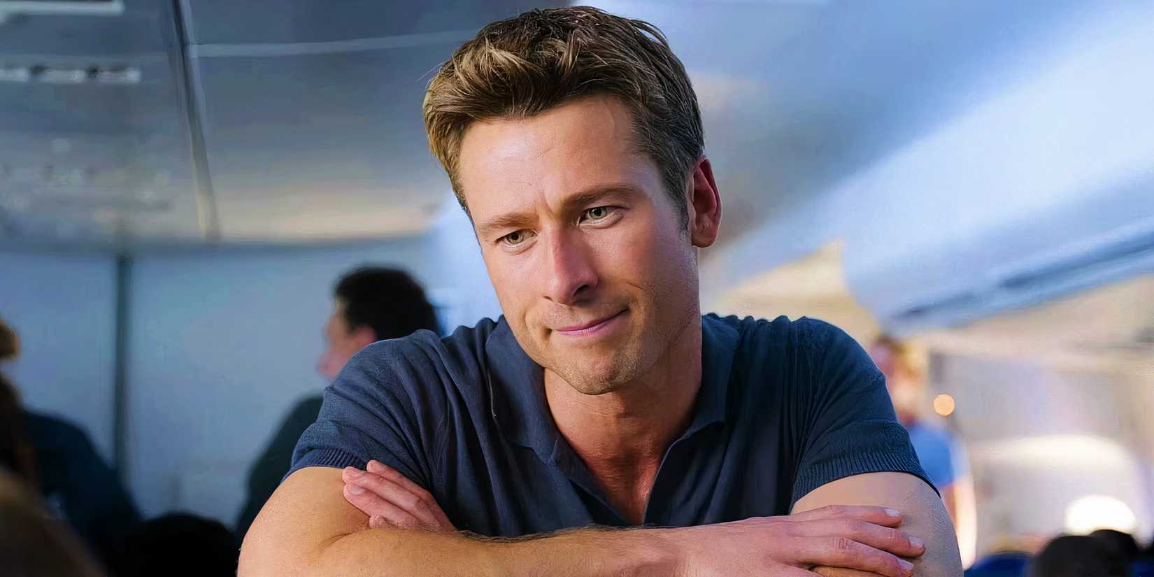 Close up of Bwn (Glen Powell) leaning over an airplane seat and facing the camera in Anyone but You.