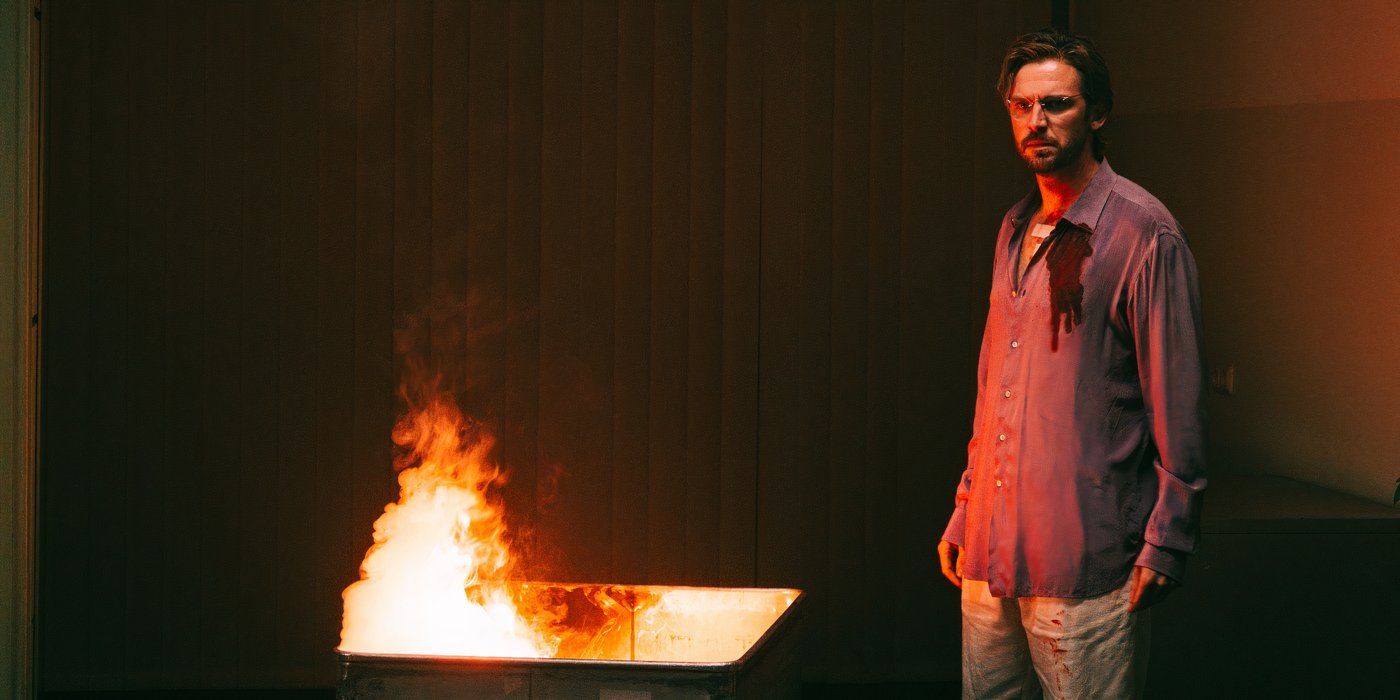 Dan Stevens com uma camisa ensanguentada em pé ao lado de uma fogueira em um contêiner em Cuckoo