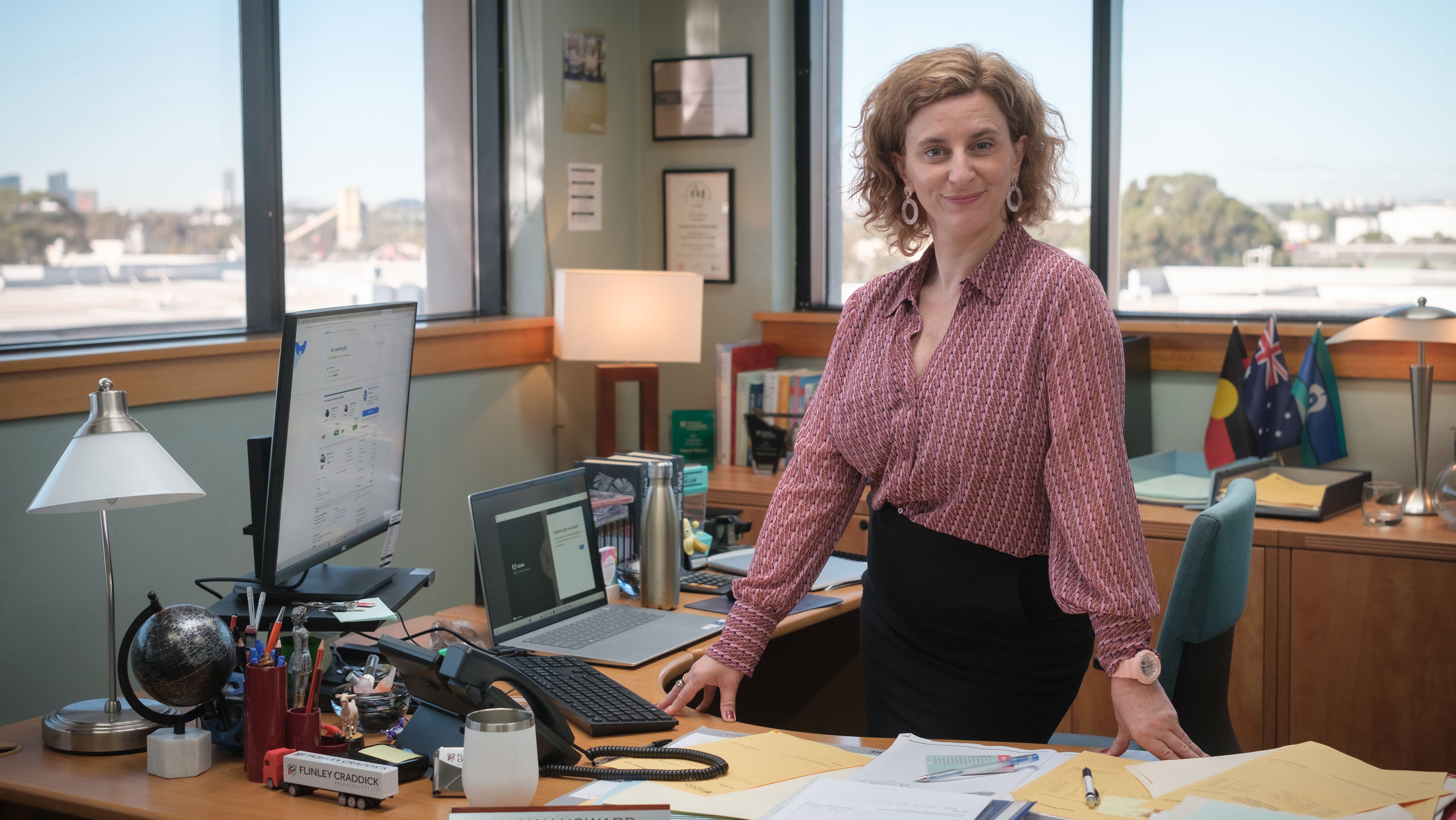 Felicity Ward as Hannah Howard sitting on a desk in Australian The Office remake