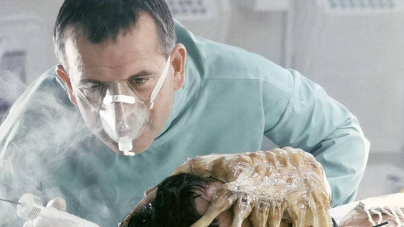 ian-holm-in-alien-inspecting-someone-with-a-facehugger-latched-onto-their-face