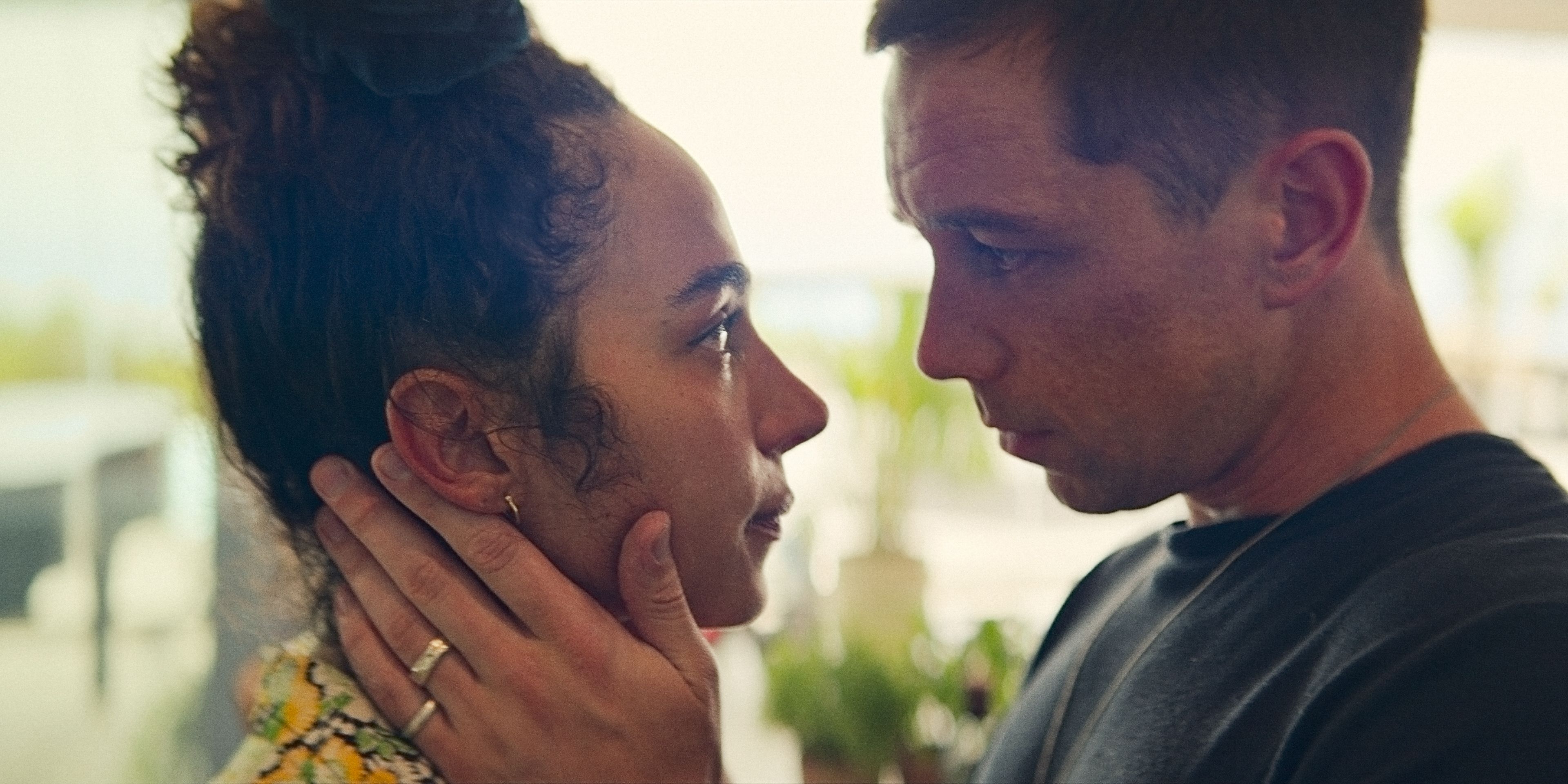 Riddy (Aurora Perrineau) e Orpheus (Killian Scott) olhando nos olhos um do outro, prestes a se beijar na 1ª temporada de KAOS