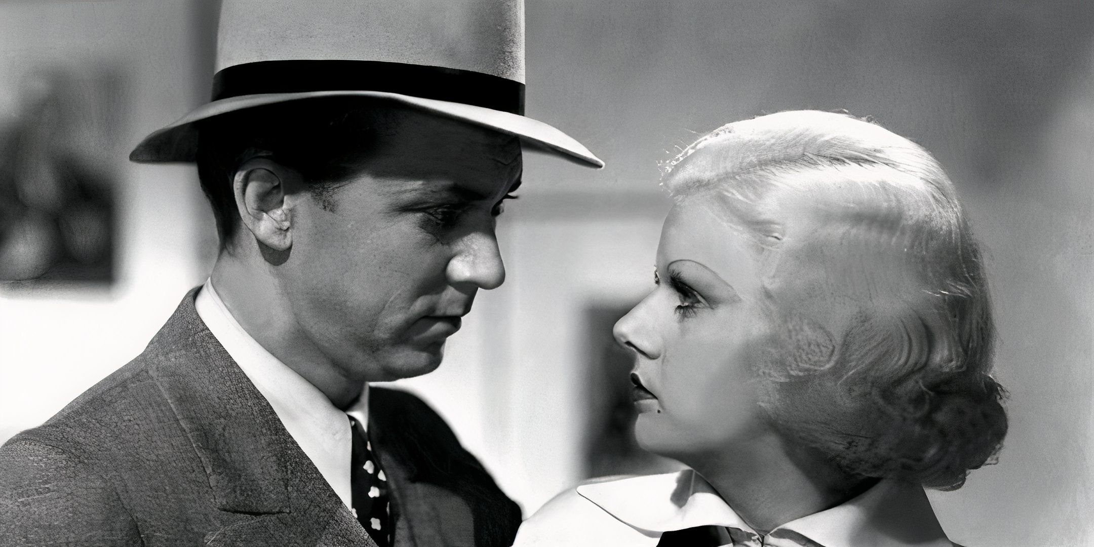 Lee Tracy segura Jean Harlow na frente dele enquanto eles olham nos olhos um do outro. 