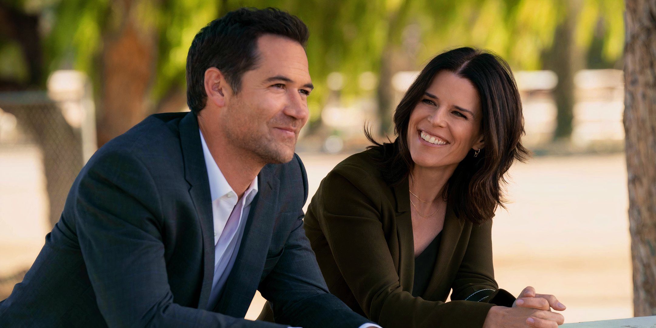 Manuel García-Rulfo como Mickey y Neve Campbell como Maggie sonríen en The Lincoln Lawyer