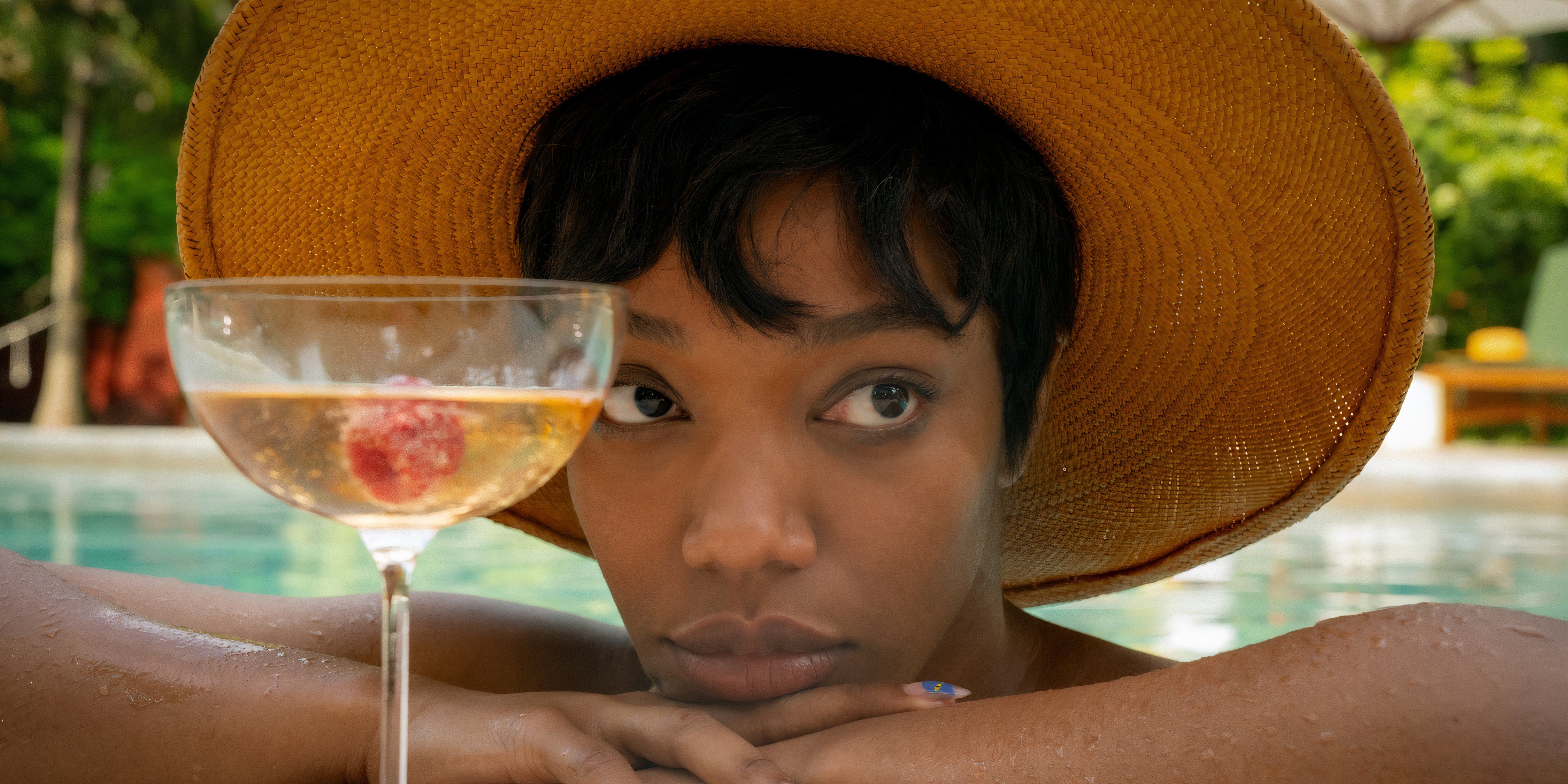 Naomie Ackie sitzt in Blink Twice in einem Schwimmbad mit Champagner vor sich