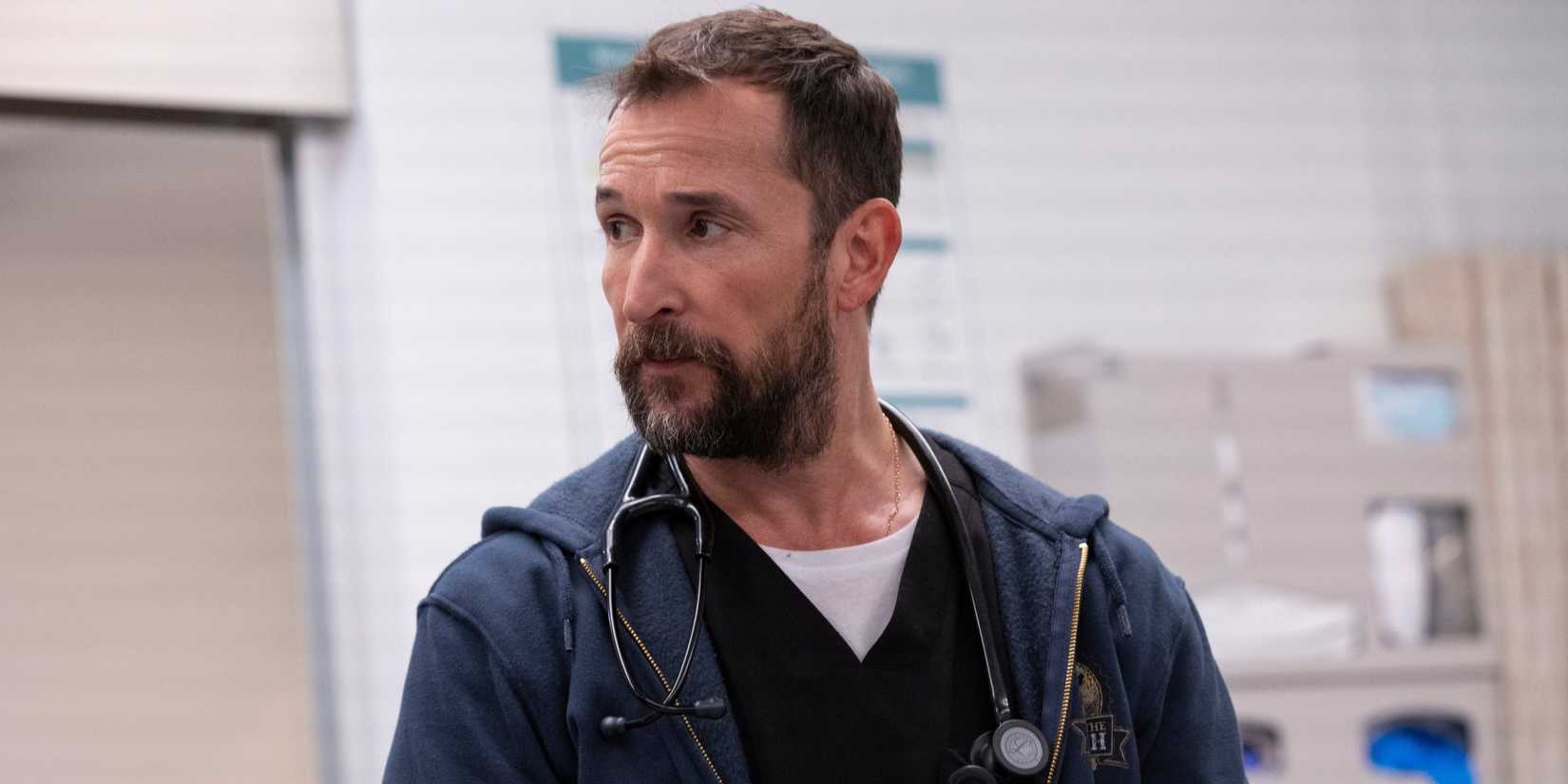 Noah Wyle in black scrubs with a blue hoodie over it, a stethoscope hanging over his neck, in The Pitt