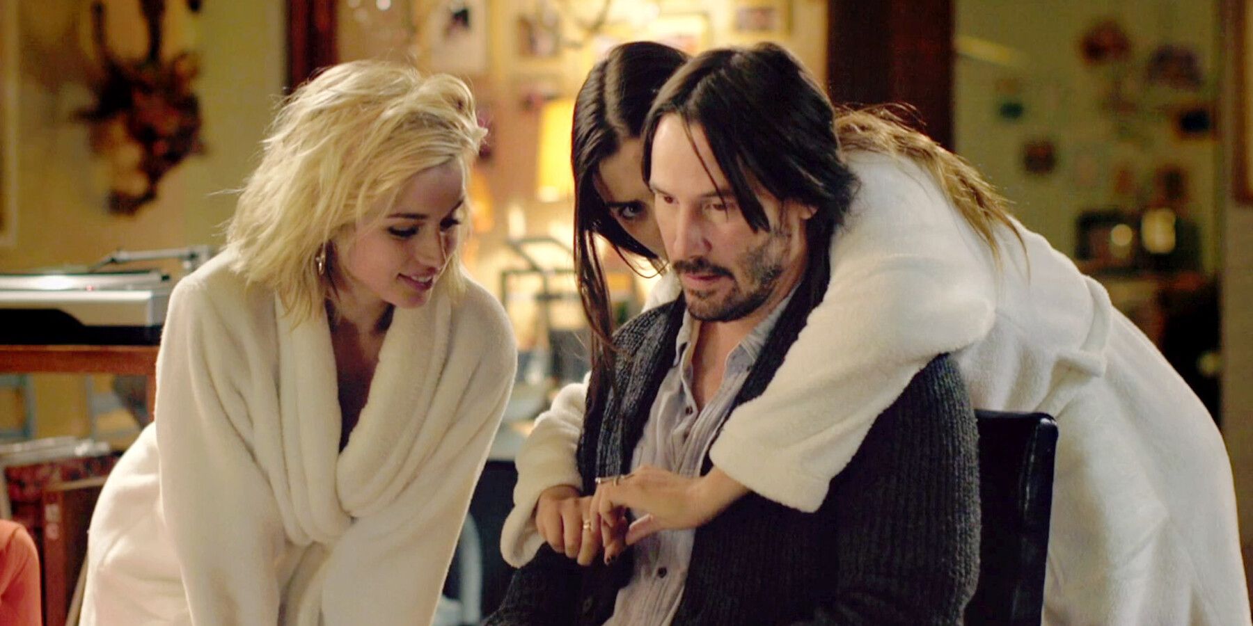 Bel (Ana de Armas) y Génesis (Lorenza Izzo) se apoyan en Evan (Keanu Reeves) en batas de baño en Knock Knock