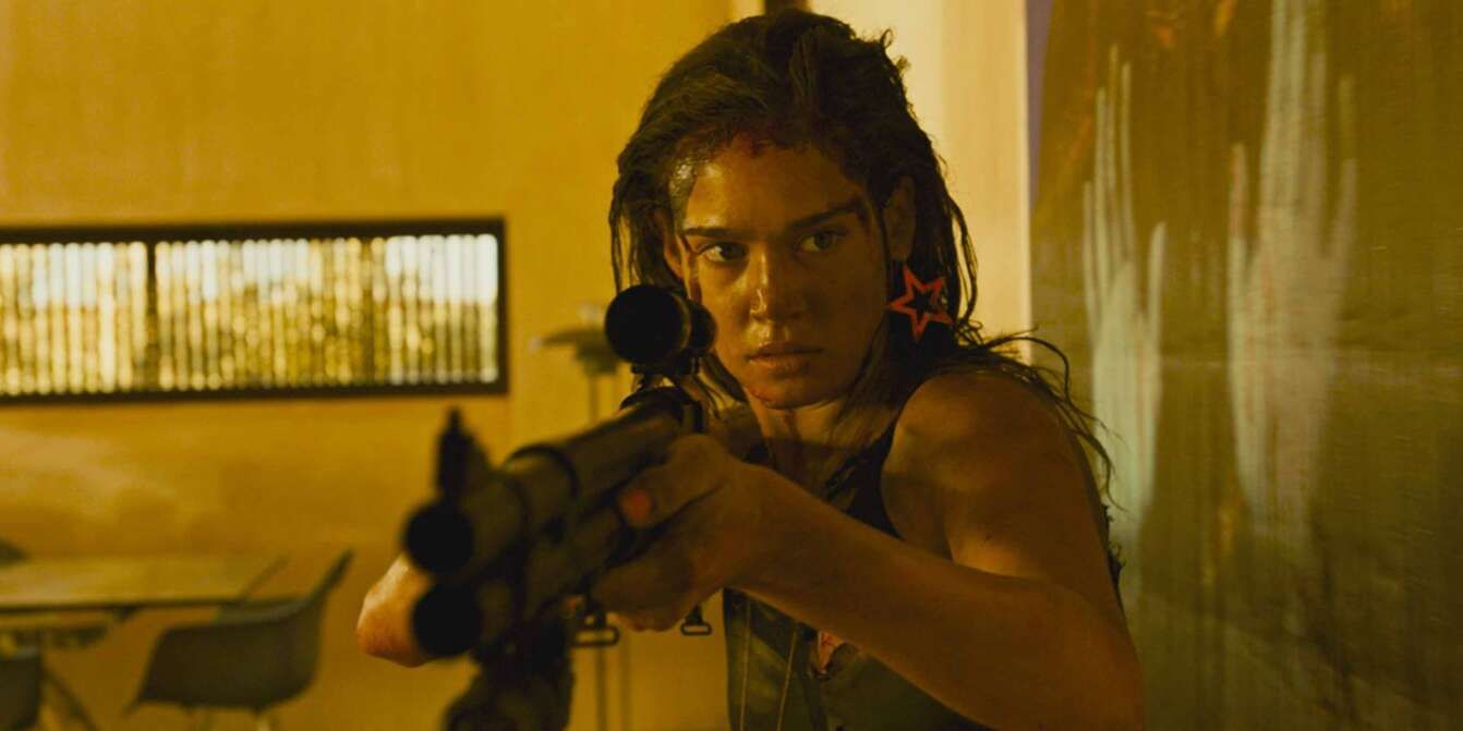 Jen (Matilda Lutz) in Revenge holding a gun as she looking warily off screen 