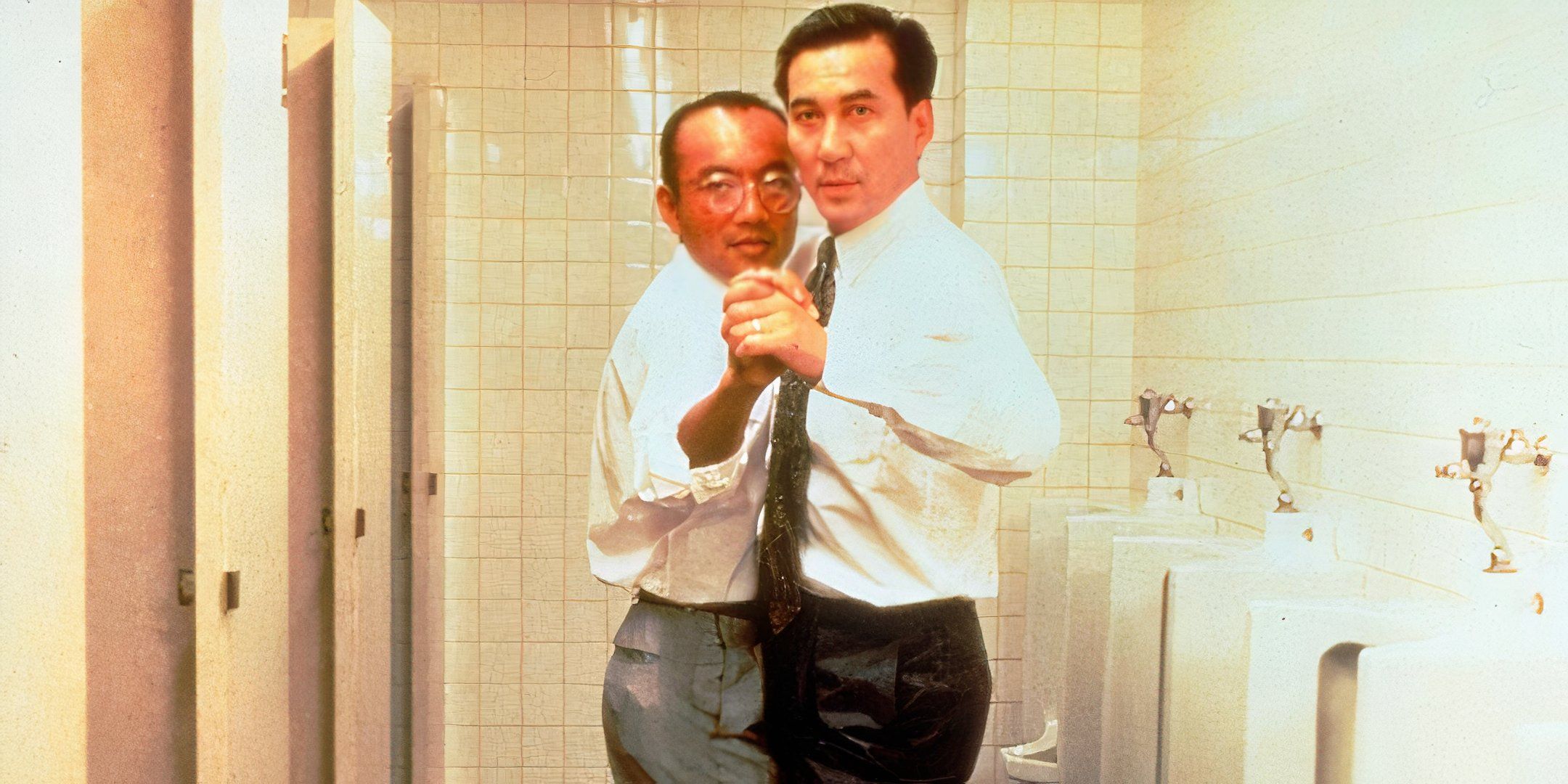 Two men dance together in a men's bathroom. 