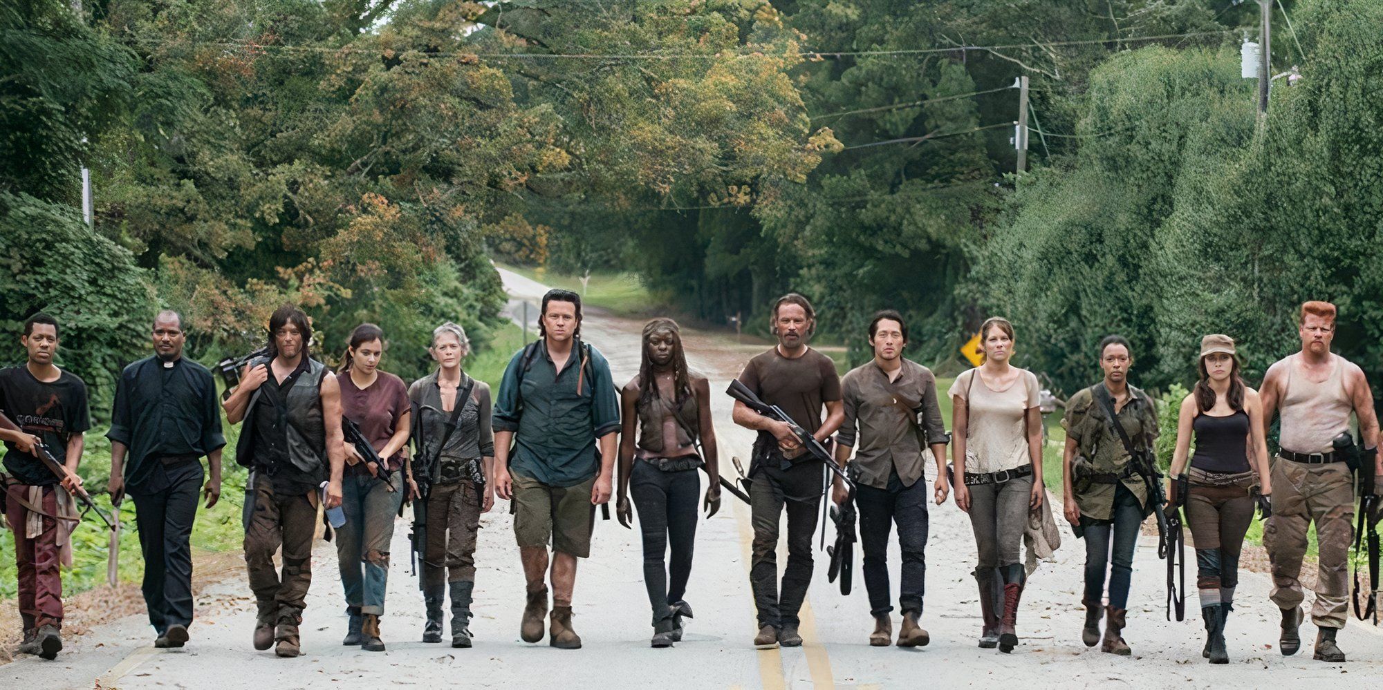The large ensemble cast of the Walking Dead walk side-by-side down a road