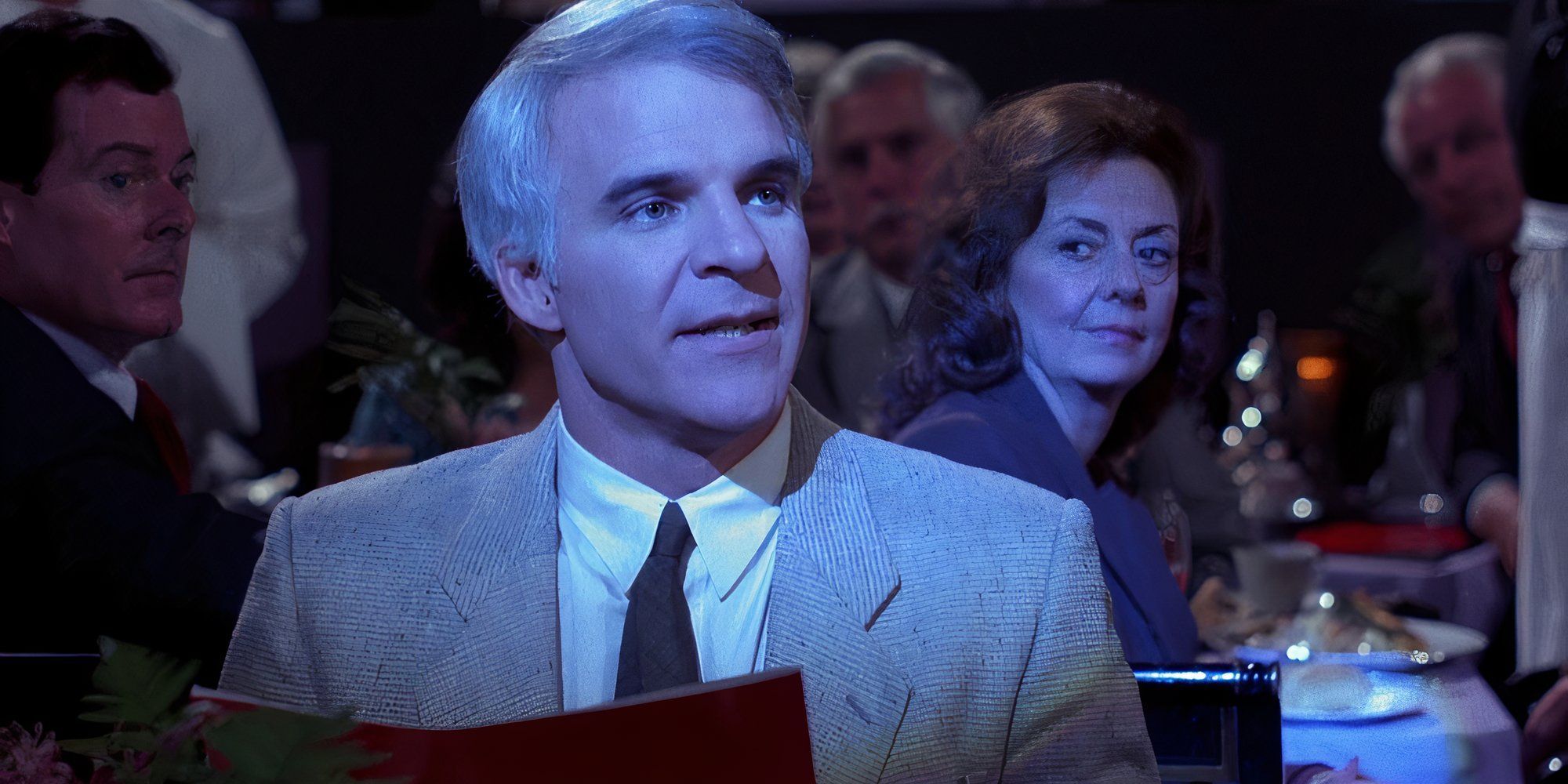 Steve Martin, como Larry Hubbard, estava sentado em um restaurante escuro sendo observado por outros clientes em The Lonely Guy. 