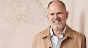 the golden bachelorette's keith smiling in a beige coat and white shirt