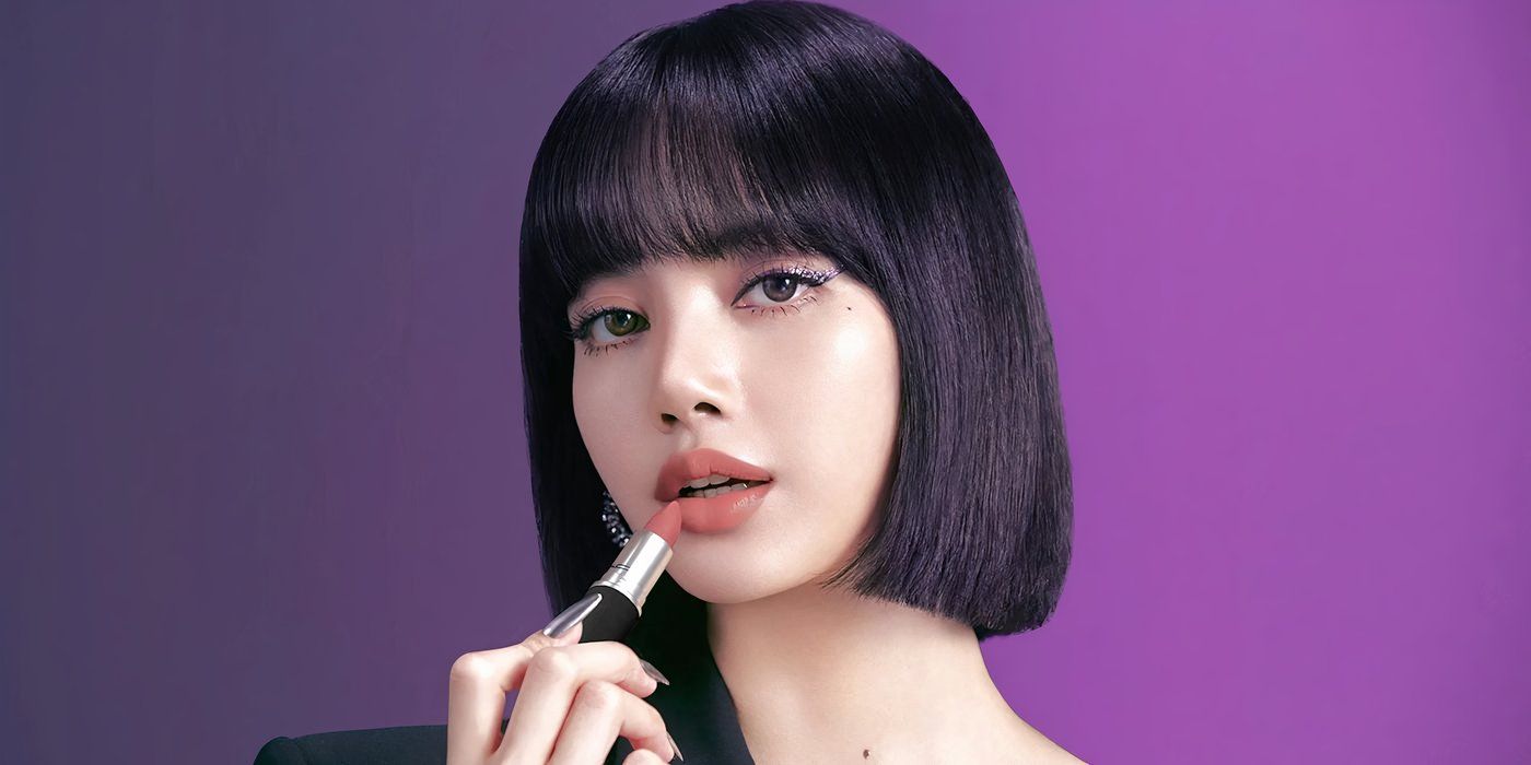 K-Pop star Lisa applies lipstick in a promo image against a purple backdrop