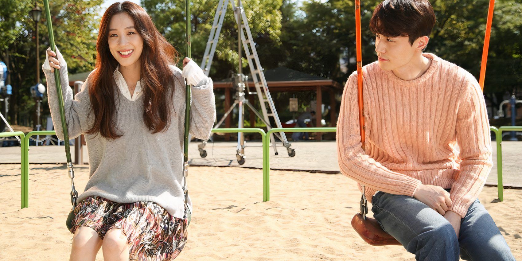 Uma jovem mulher e um jovem sentados em balanços no parque no K-drama Bubble Gum