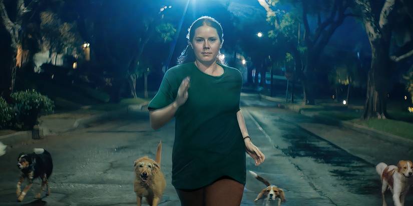 Mother (Amy Adams) runs down a street chased by dogs in Nightbitch.