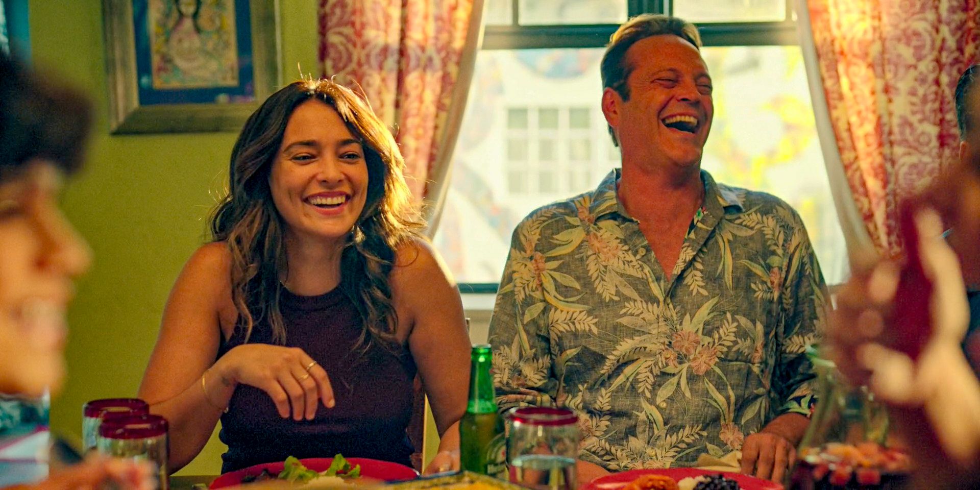 Rosa (Natalie Martinez) and Yancy (Vince Vaughn) laughing out loud during a family meal with Rosa's family in Bad Monkey Season 1 Episode 5