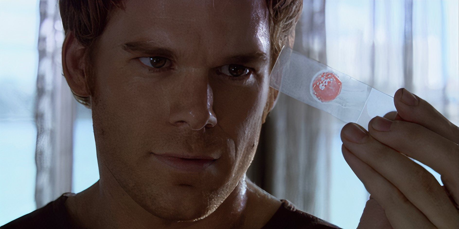 Dexter Morgan (Michael C. Hall) sonríe sobre un portaobjetos de sangre en Dexter Temporada 1, Episodio 1