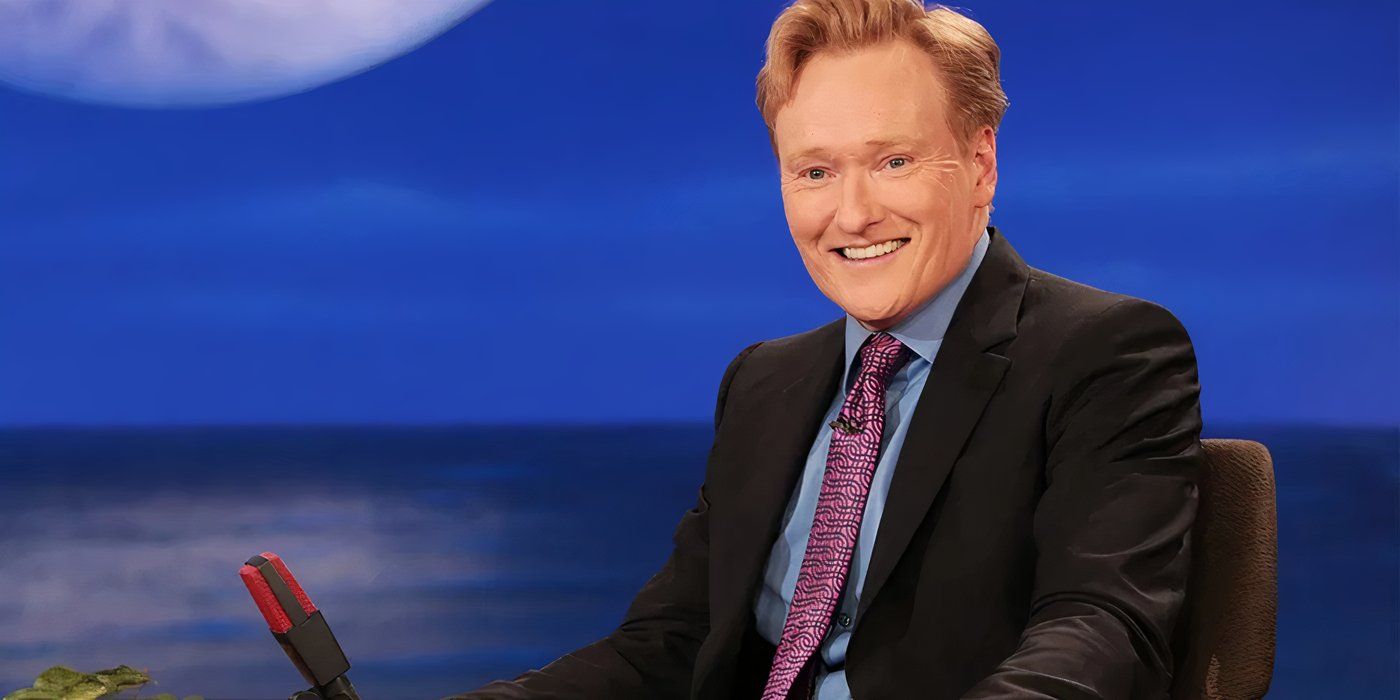 Conan O'Brien smiling behind a desk as he hosts a late-night talk show