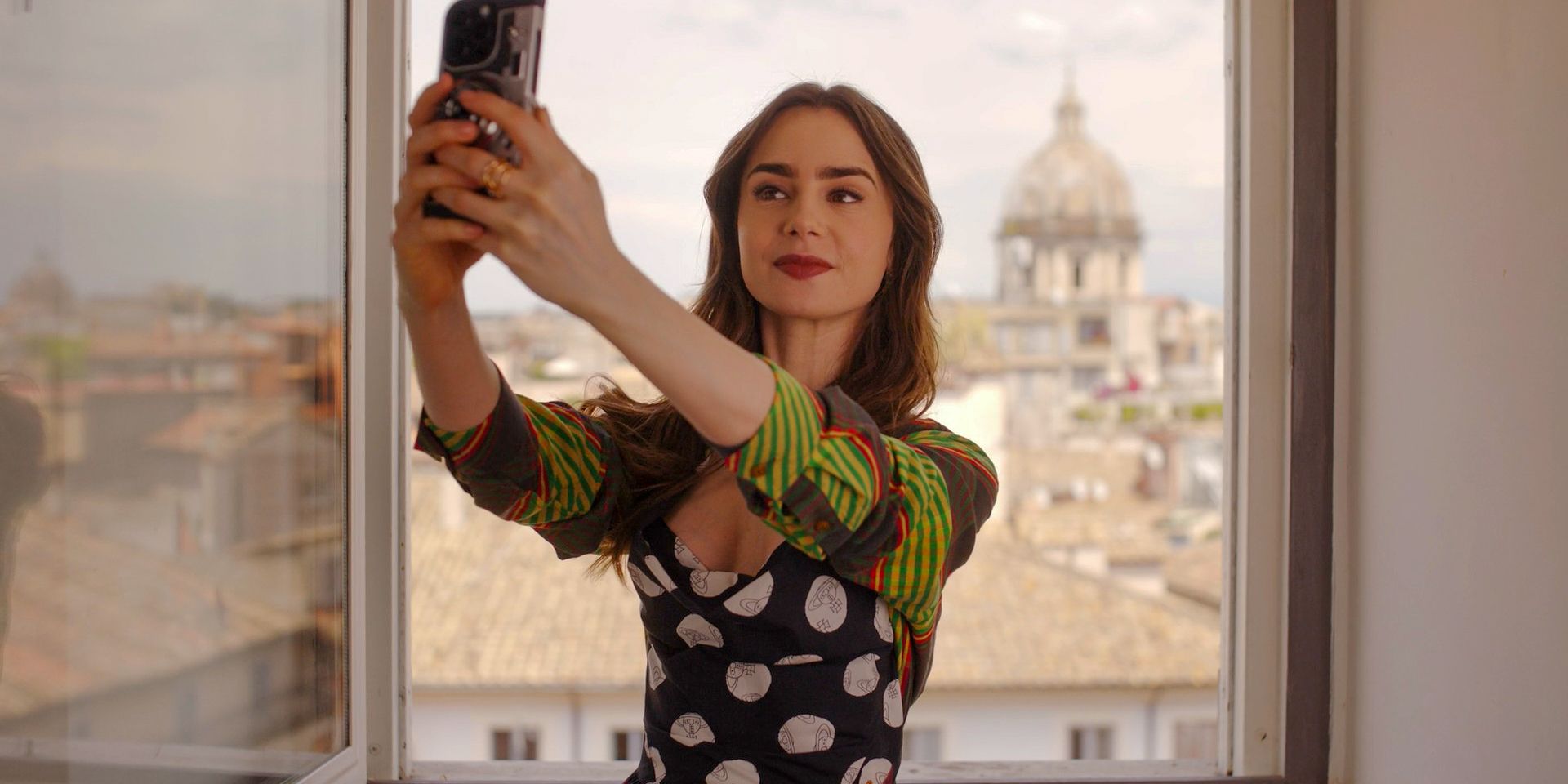 Emily taking a photo of herself next to an open window in Emily in Paris Season 4 Episode 10