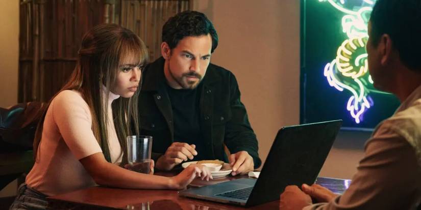 Giacomo Gianniotti as Cole Ellis and Vanessa Morgan as Max Mitchell working on a laptop together in Wild Cards.