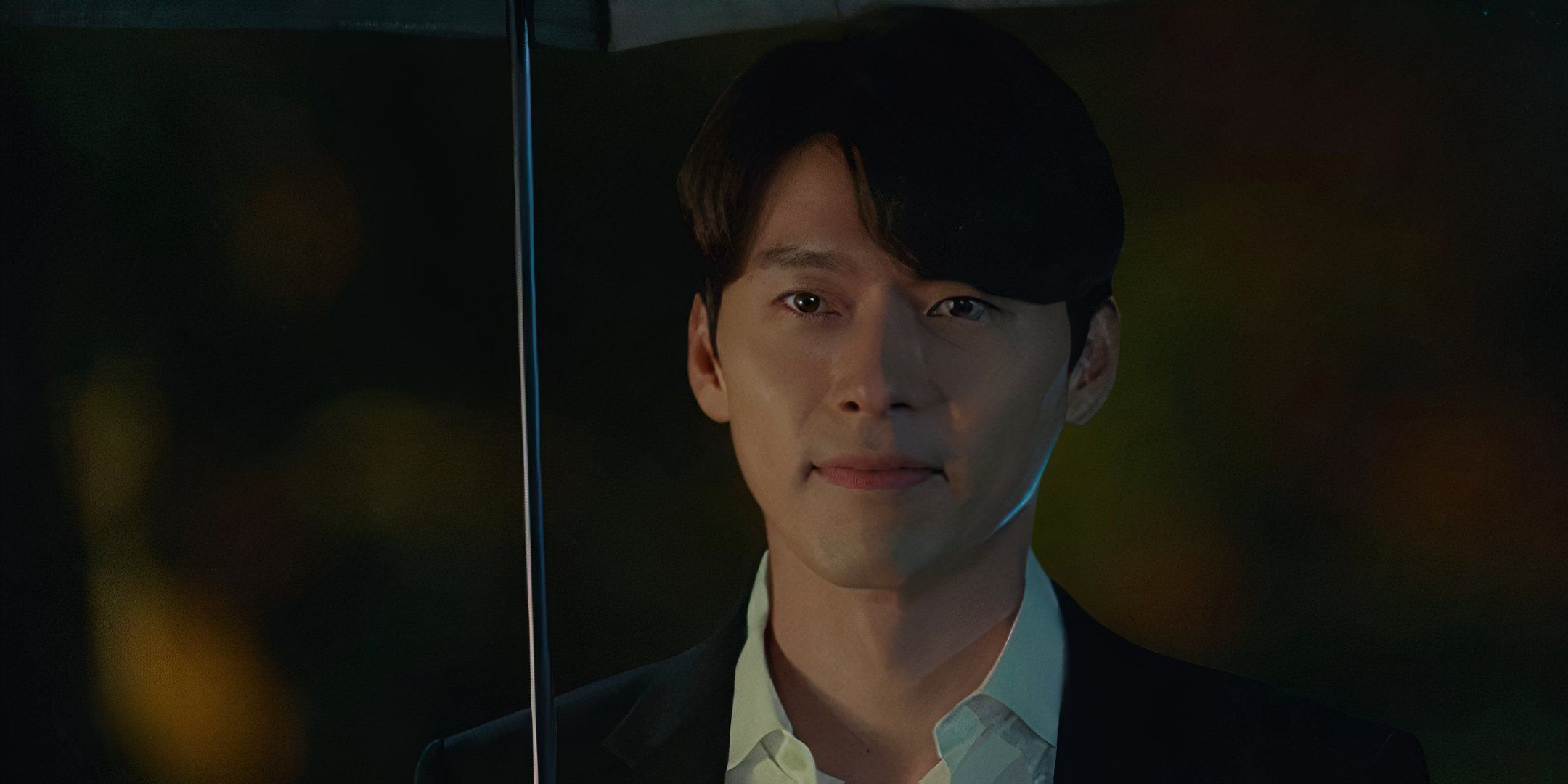 Hyun Bin stands outside underneath an umbrella. 