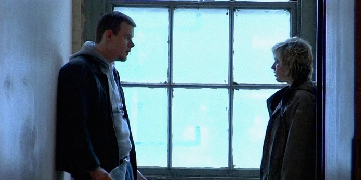 Joe Swanberg and Greta Gerwig talking in a hallway against a window.