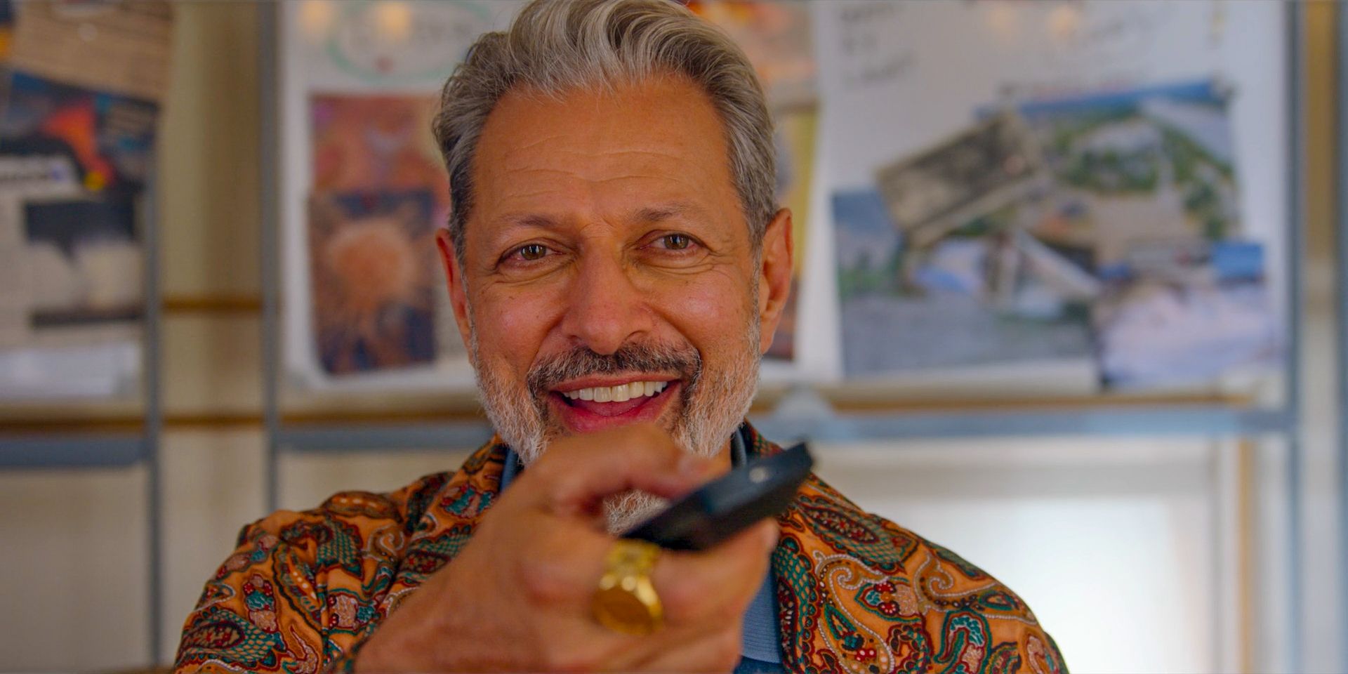 Zeus (Jeff Goldblum) sonríe y presiona el control remoto de su televisor.