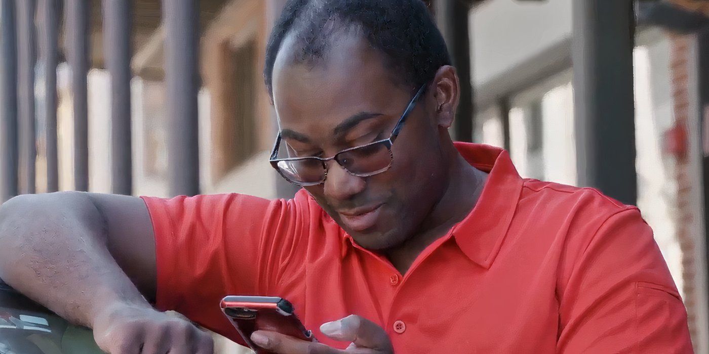 Niles Valentine In 90 Day Fiance in orange shirt looking into phone