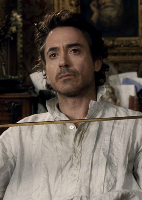 Robert Downey Jr. as Sherlock Holmes in Sherlock Holmes (2009) sitting in a chair while holding a violin bow