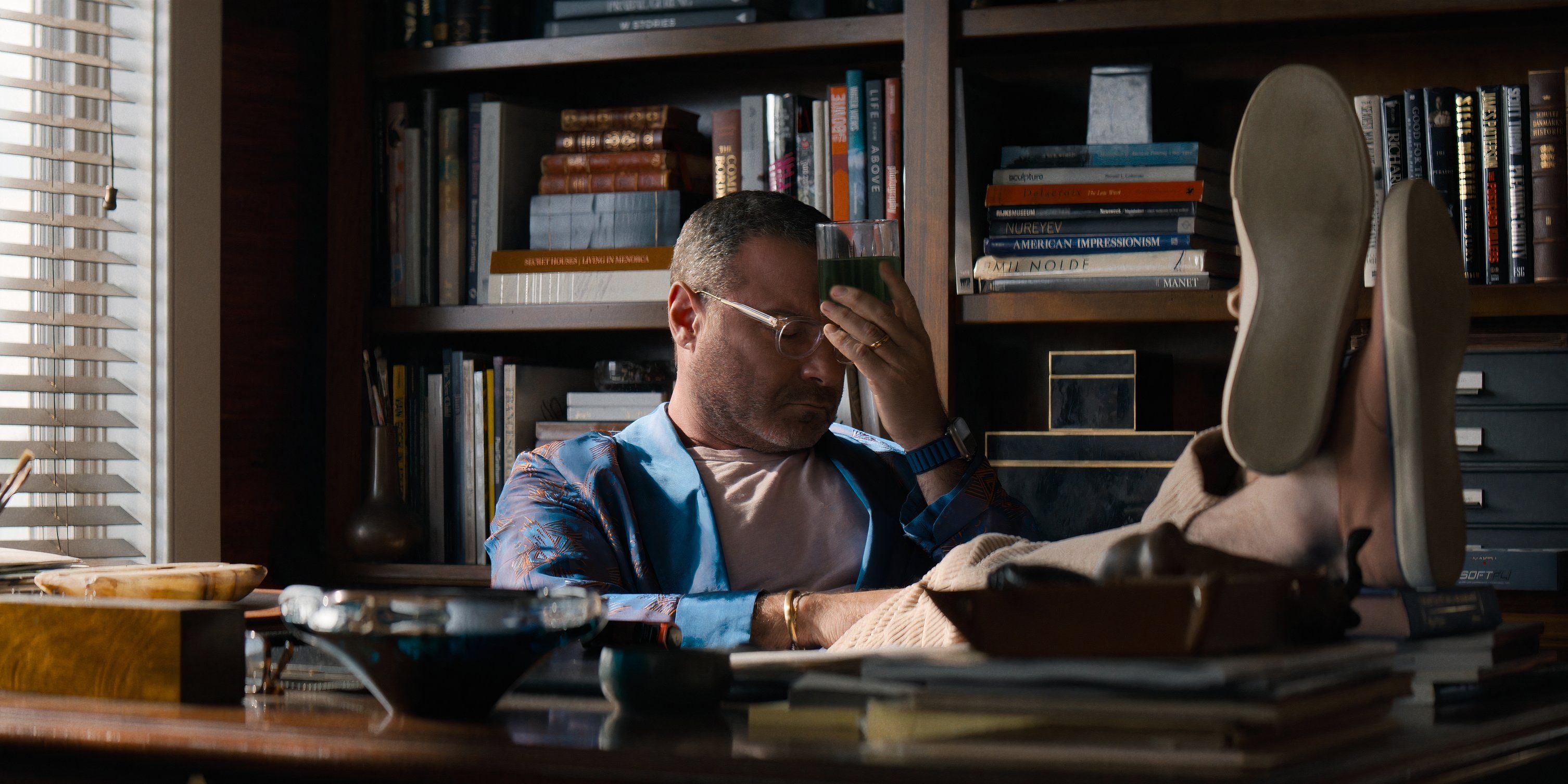 Tag pinches the bridge of his nose while propping his feet up on his desk in The Perfect Couple episode 6