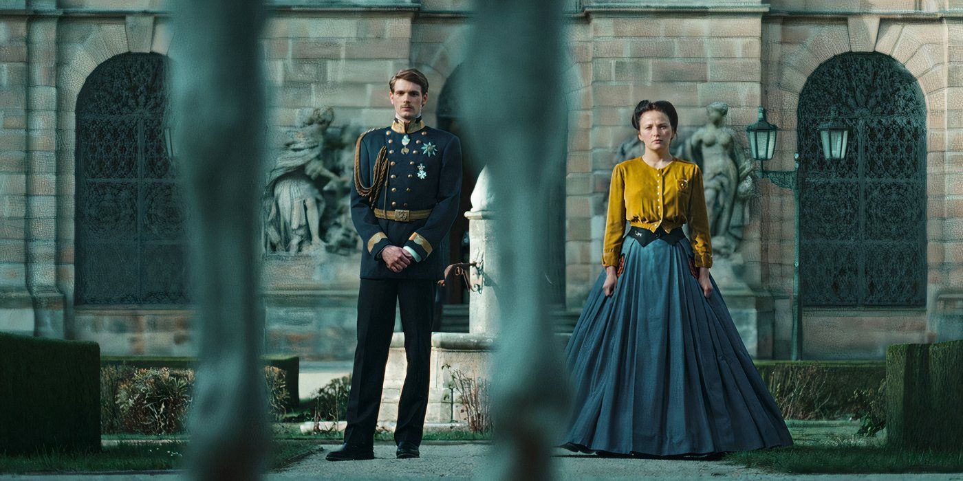 Elisabeth and Franz stand outside the palace while framed through the bars of the fence in The Empress