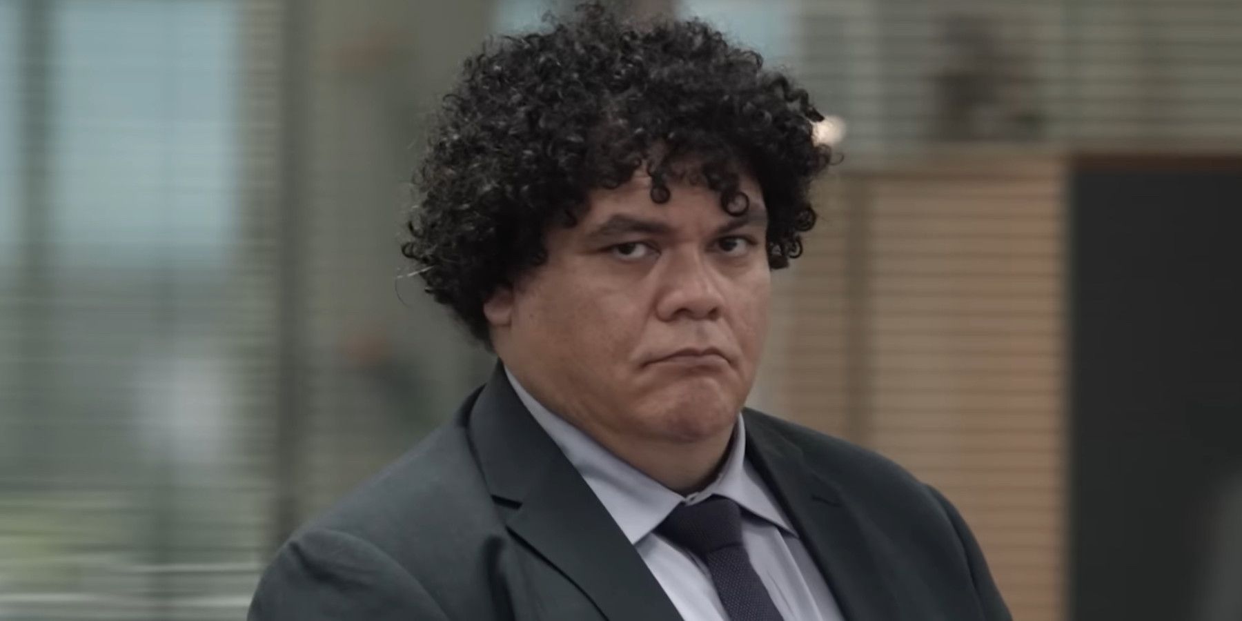 The Office Australia image of disgruntled man with curly black hair wearing a suit 