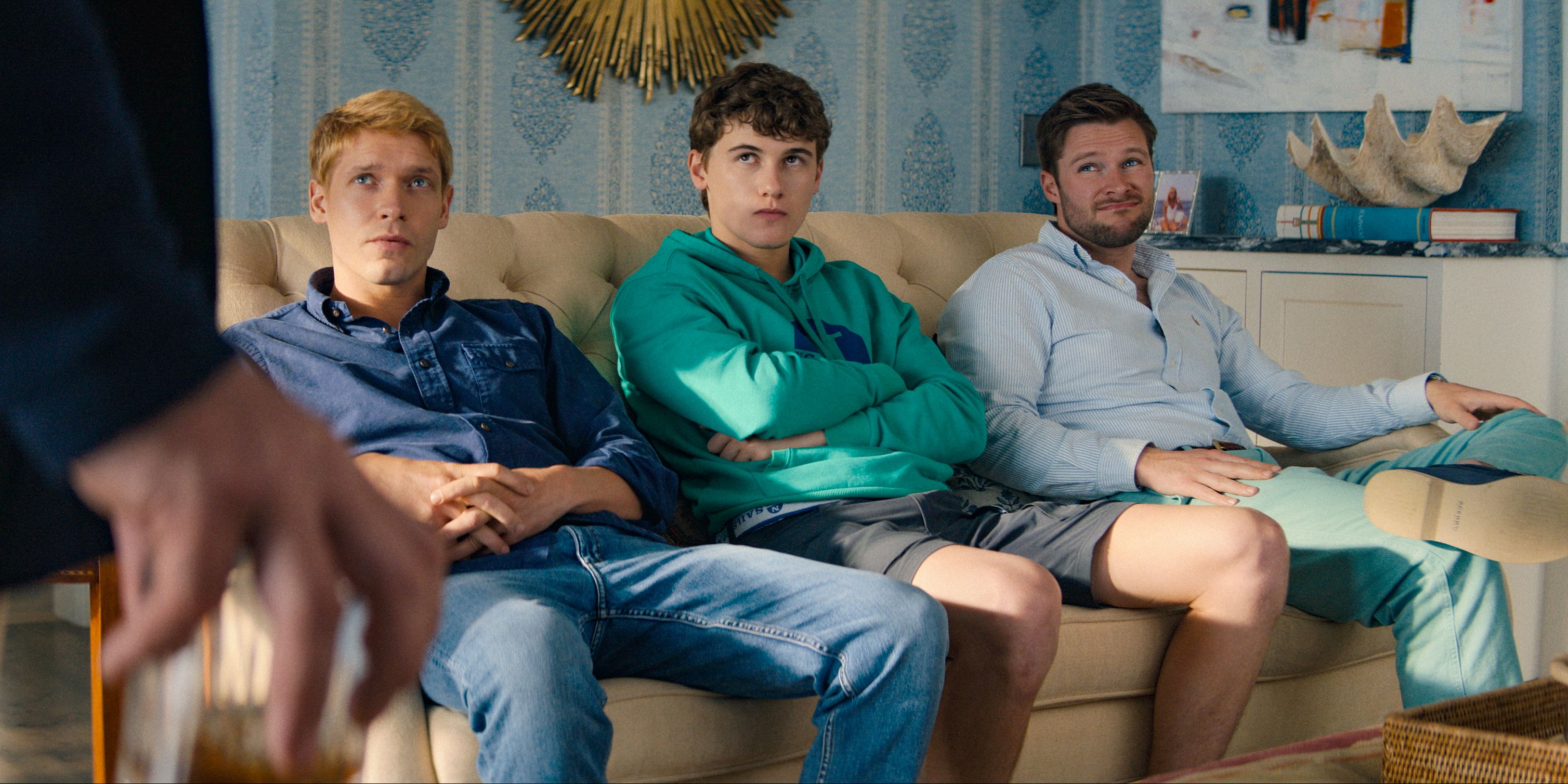 Benji Winbury (Billy Howle), Will Winbury (Sam Nivola) and Benji Winbury (Billy Howle) sitting on the couch, receiving a warning in The Perfect Couple 