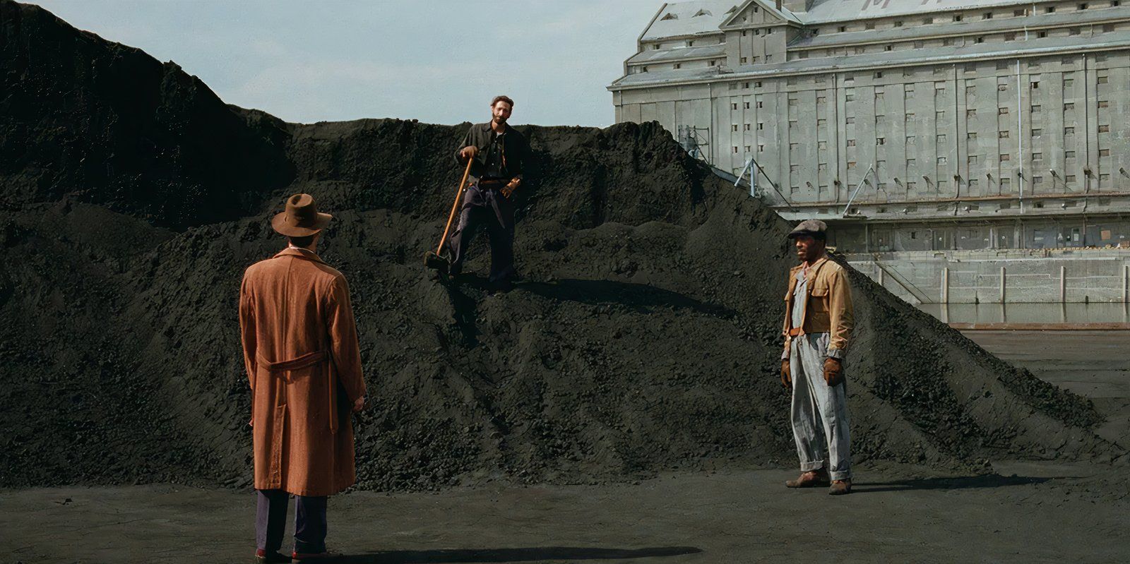 Adrian Brody stands atop a pile of dirt as László Tóth looking at two other men in The Brutalist