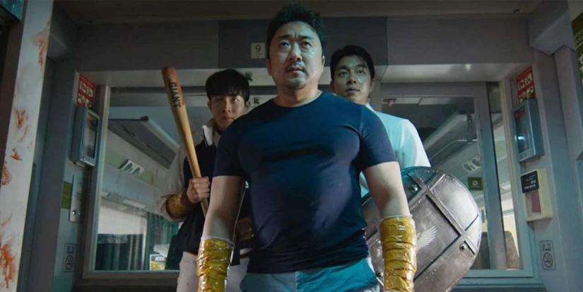 Sang-hwa stands centre frame, his arms wrapped in tape looking ahead in train to Busan