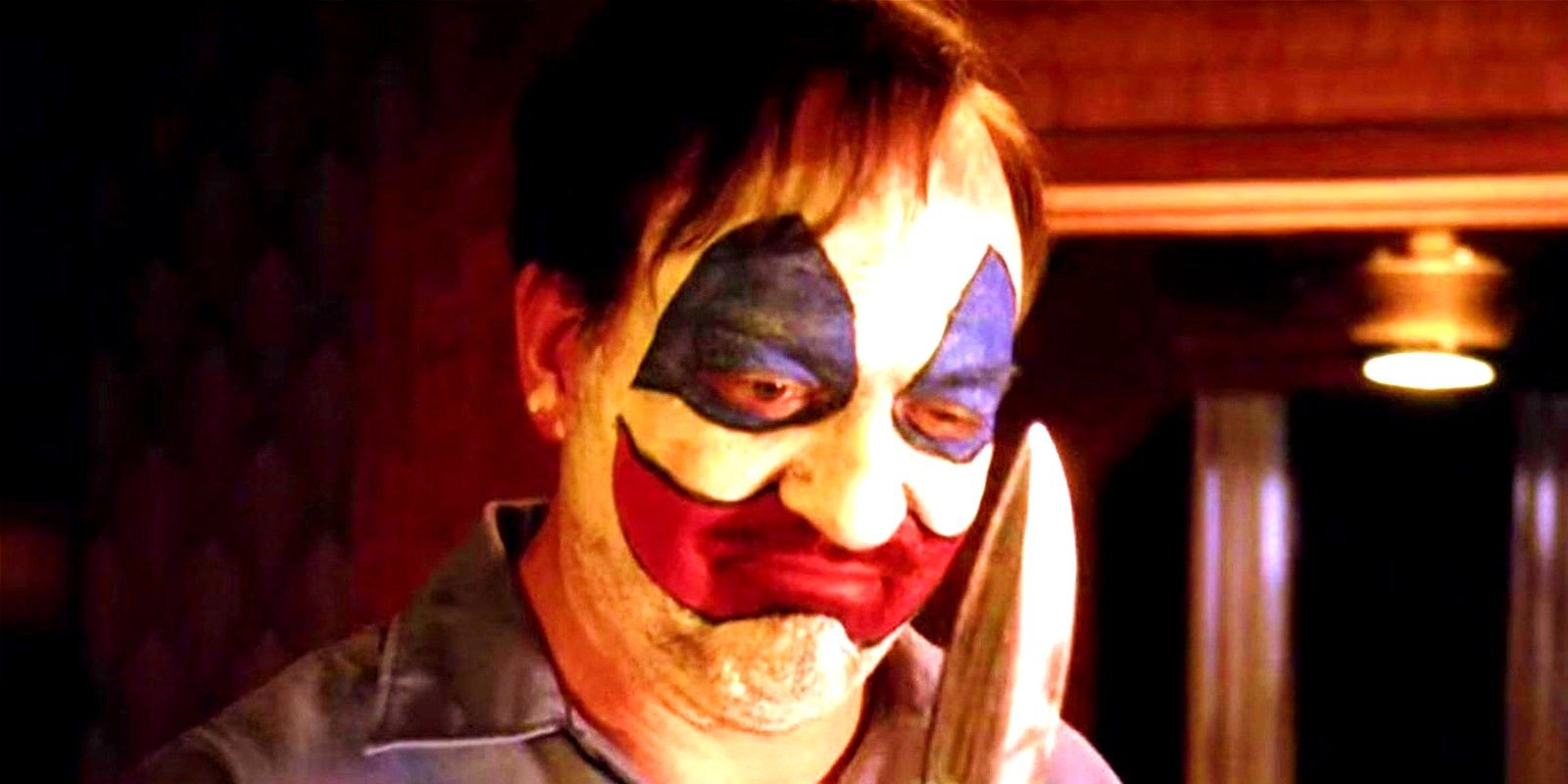 John Carroll Lynch as John Wayne Gacy holding a knife with clown makeup in American Horror Story