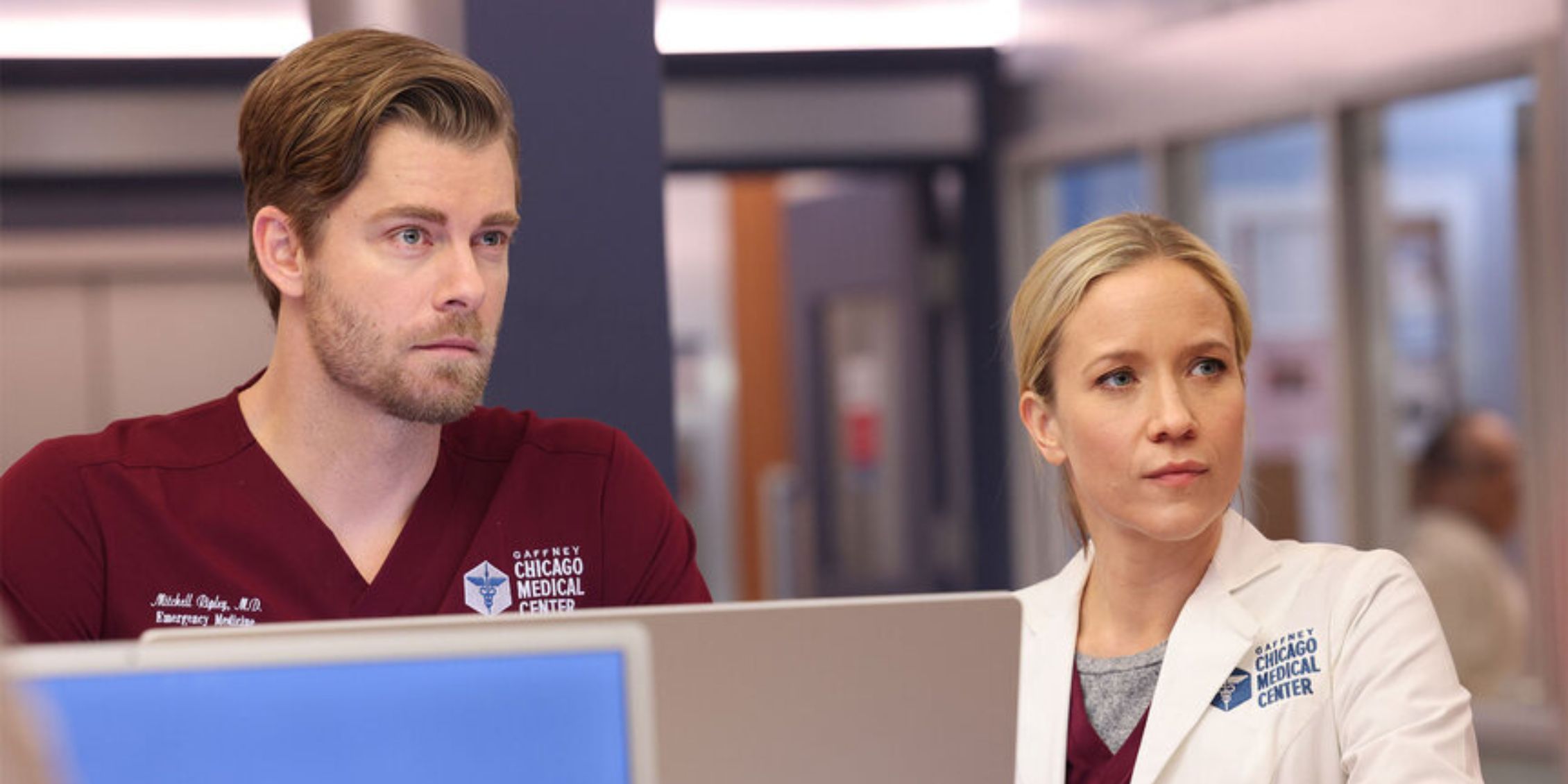 Chicago Med Hannah and Mitch standing at the nurses' station staring at something off-screen