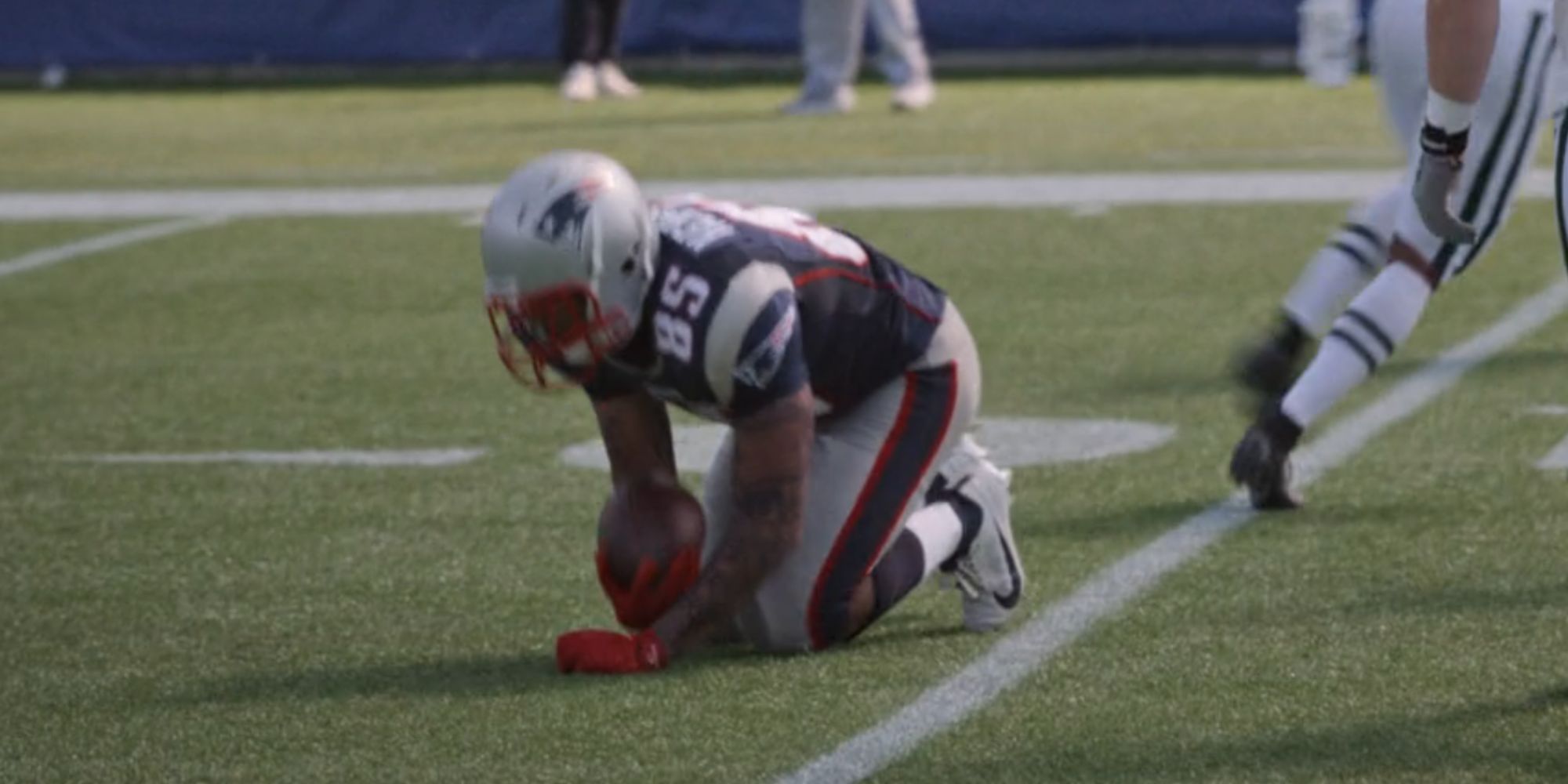 Josh Rivera as Aaron Hernandez in American Sports Story kneeling with the football